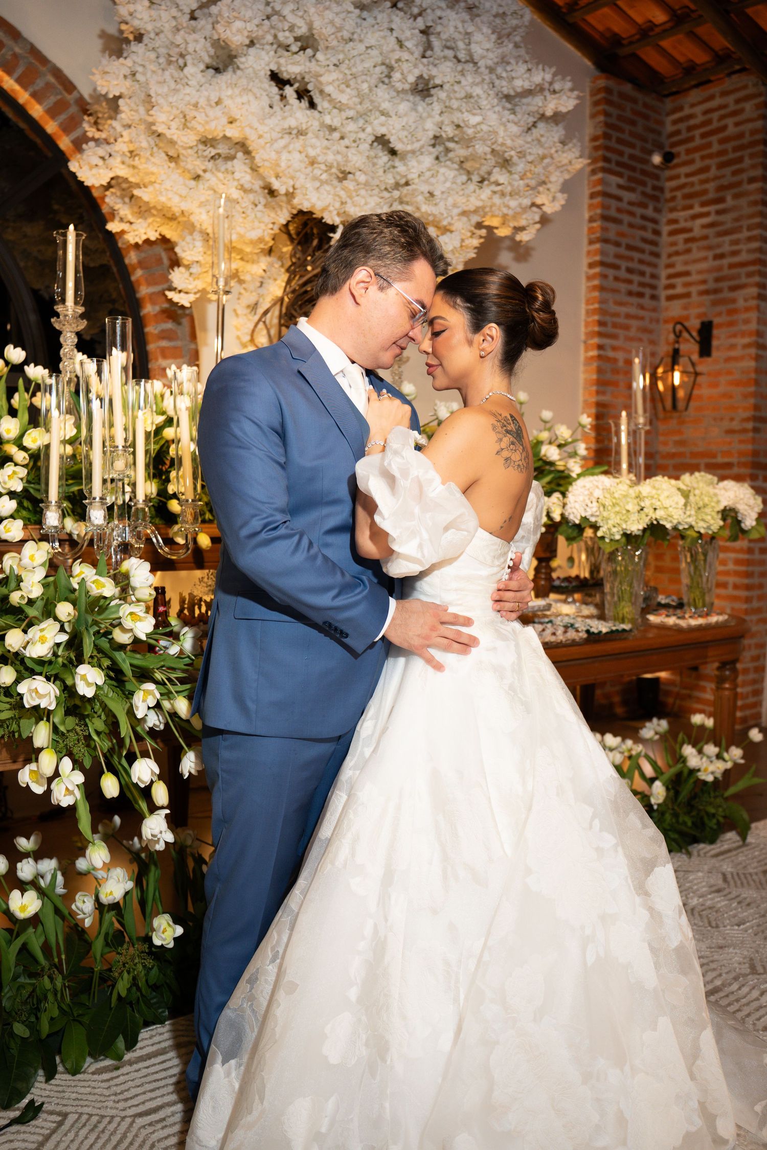 Bride and groom share romantic moment at elegant wedding reception with white floral arrangements and candlelight.