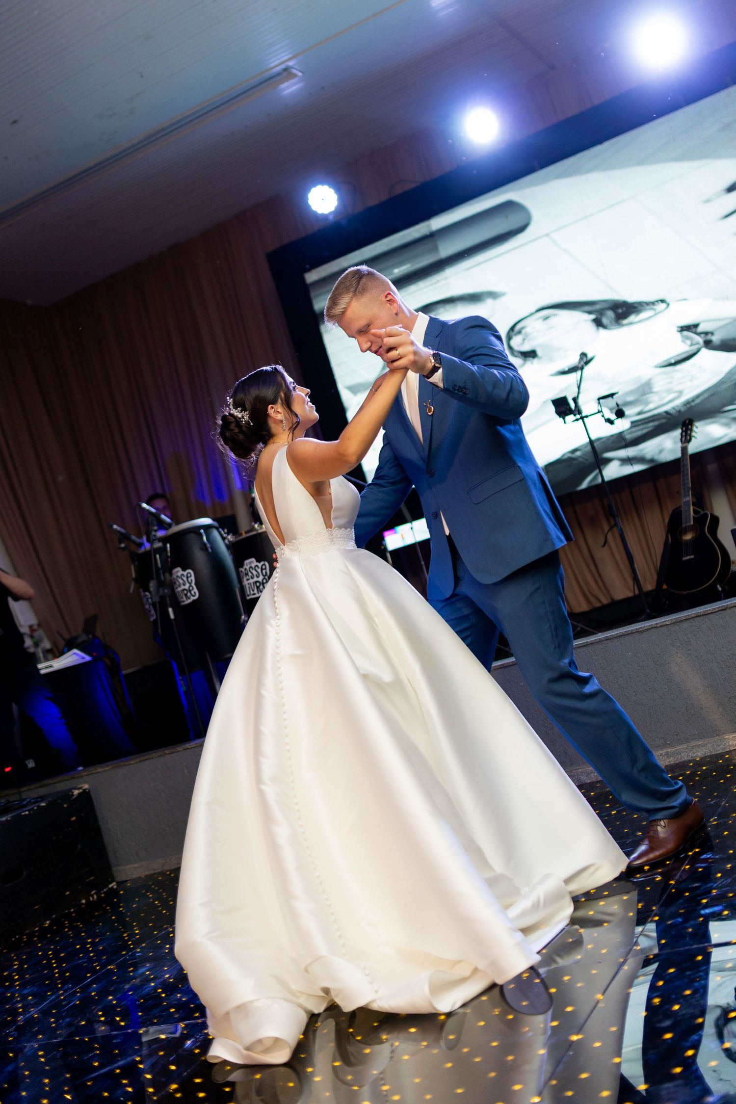 Bride in white ballgown and groom in blue suit share their first dance at elegant wedding reception.