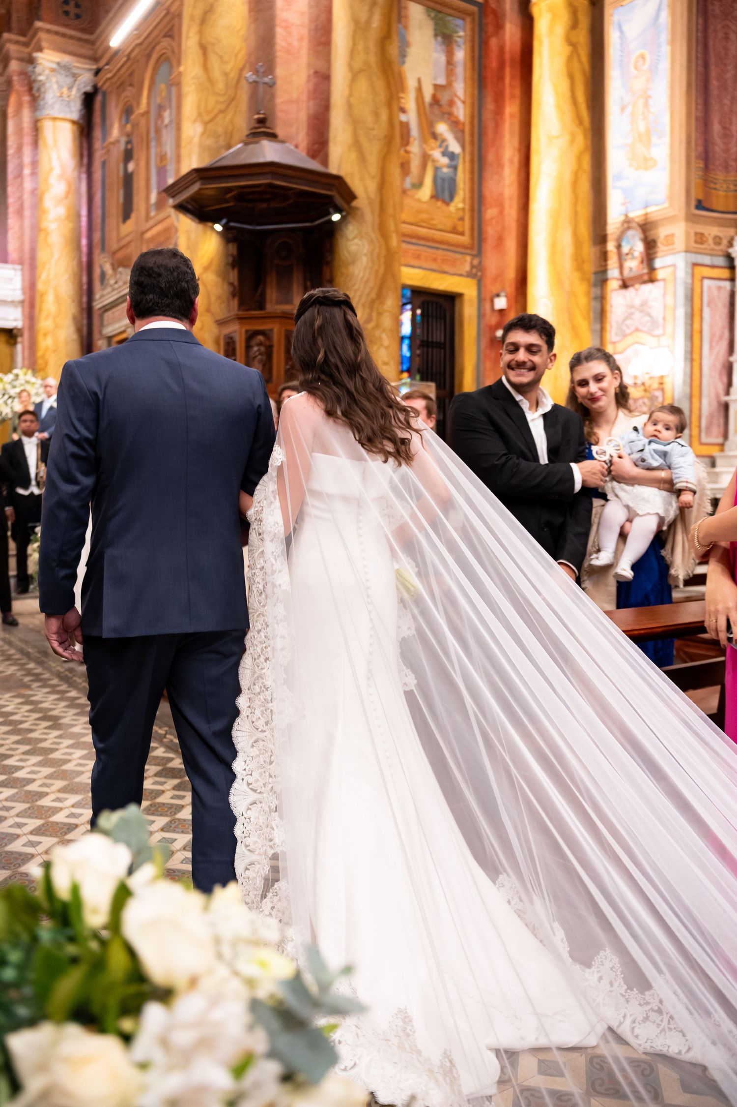 Bride in lace veil walks church aisle with groom during elegant wedding ceremony.