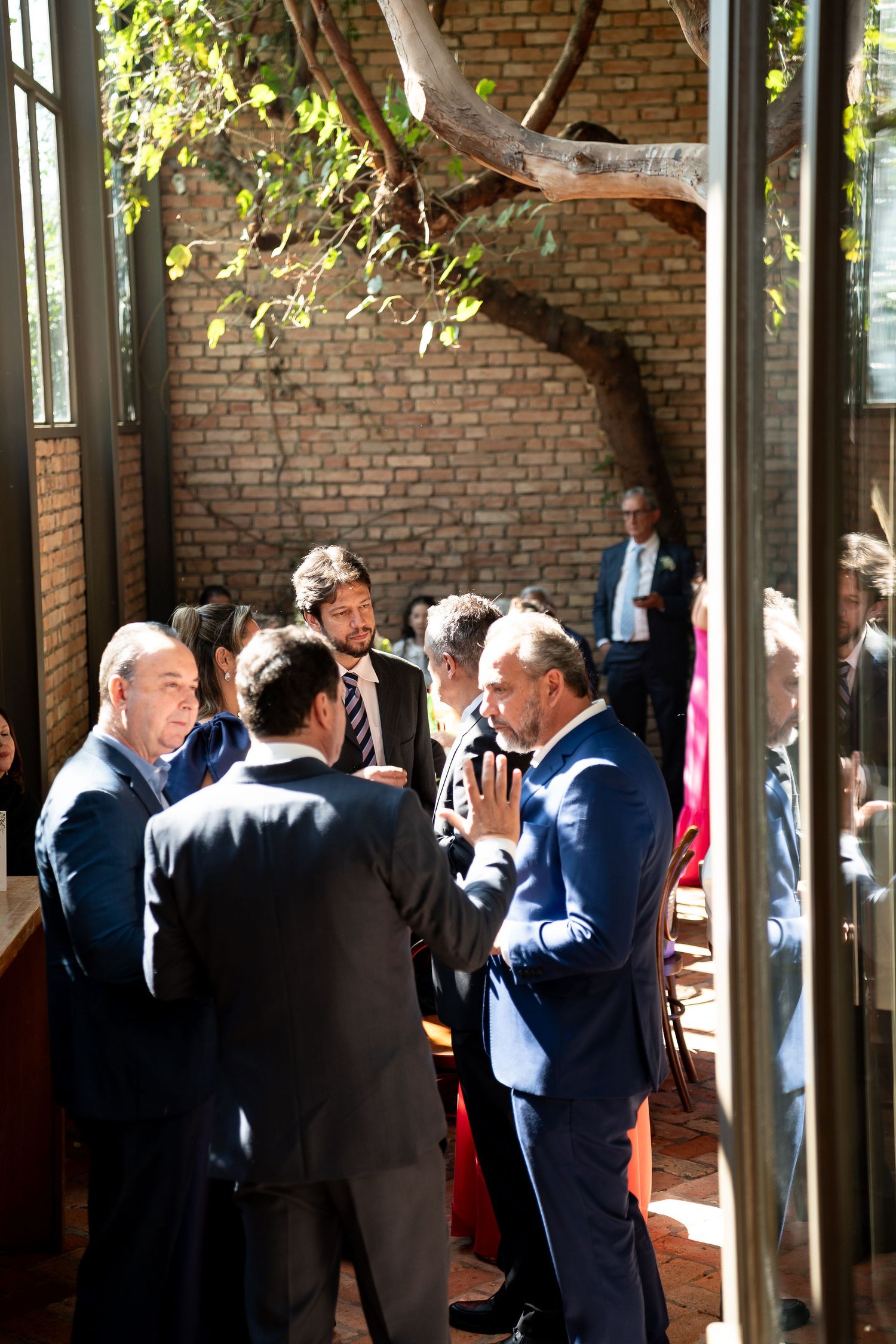 Business professionals in suits networking at an outdoor brick courtyard event during daytime.