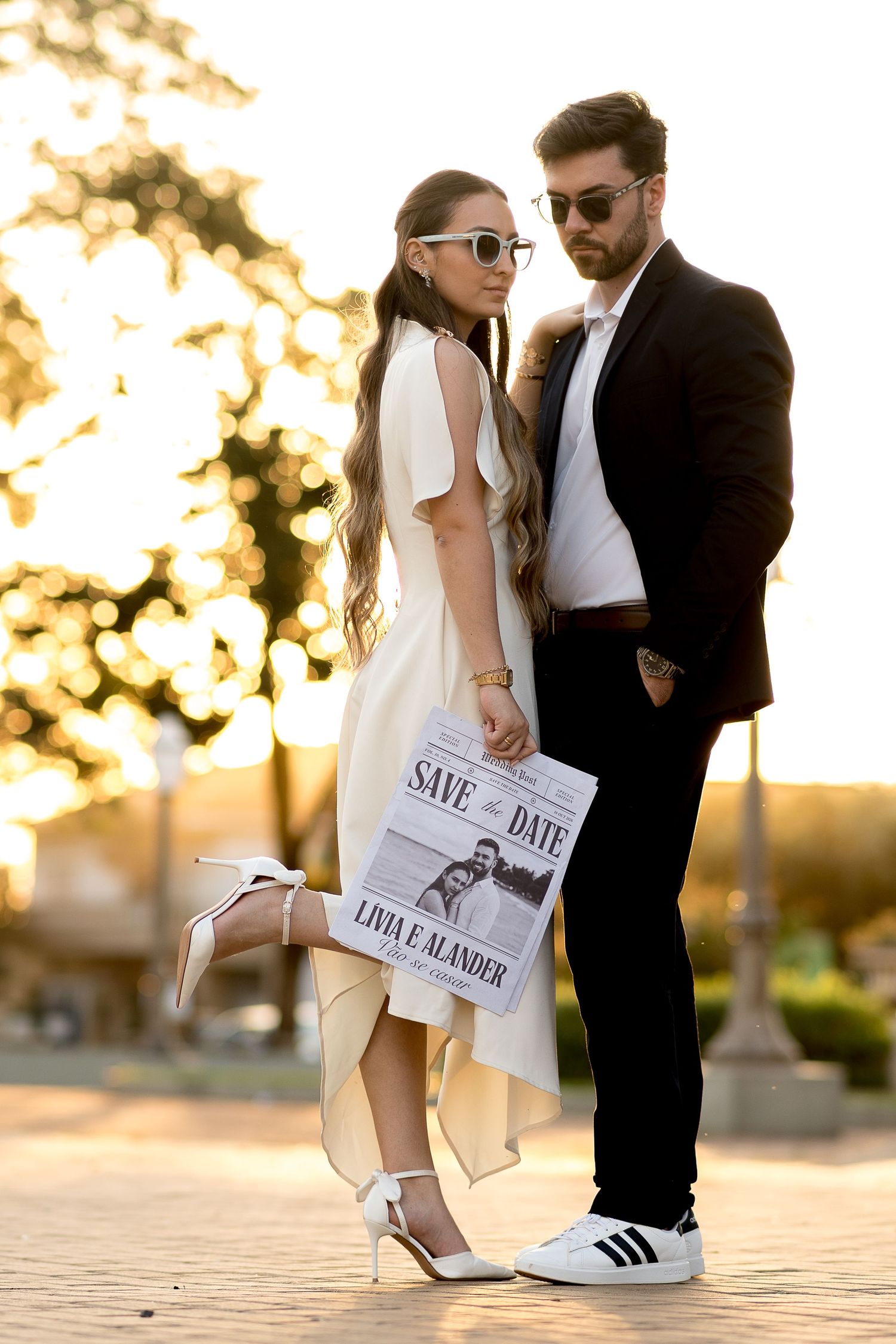 Elegant couple posing outdoors at golden hour, holding a Save the Date card for Livia and Alander's wedding.