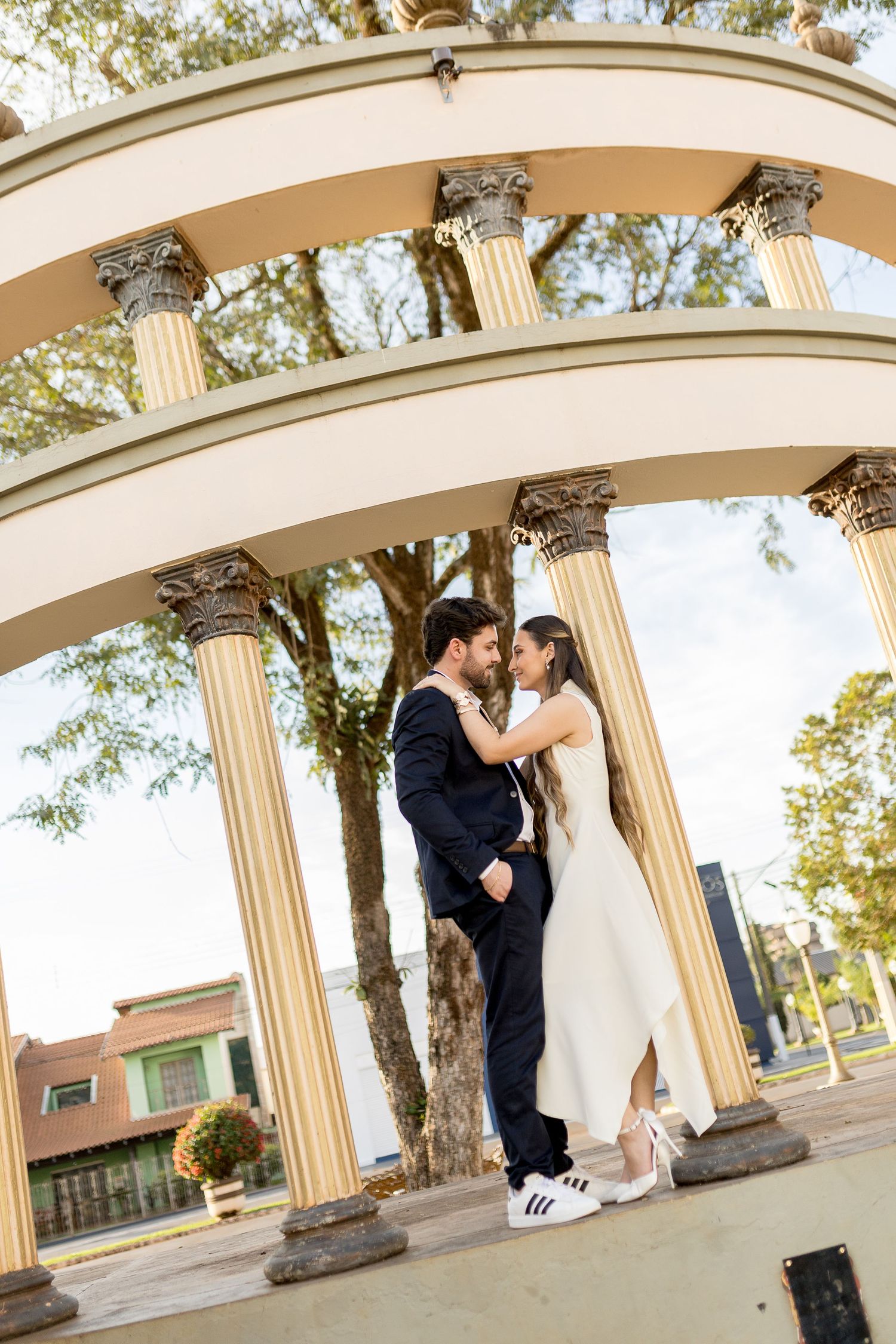 Bride and groom embrace under elegant arched gazebo with columns outdoors.