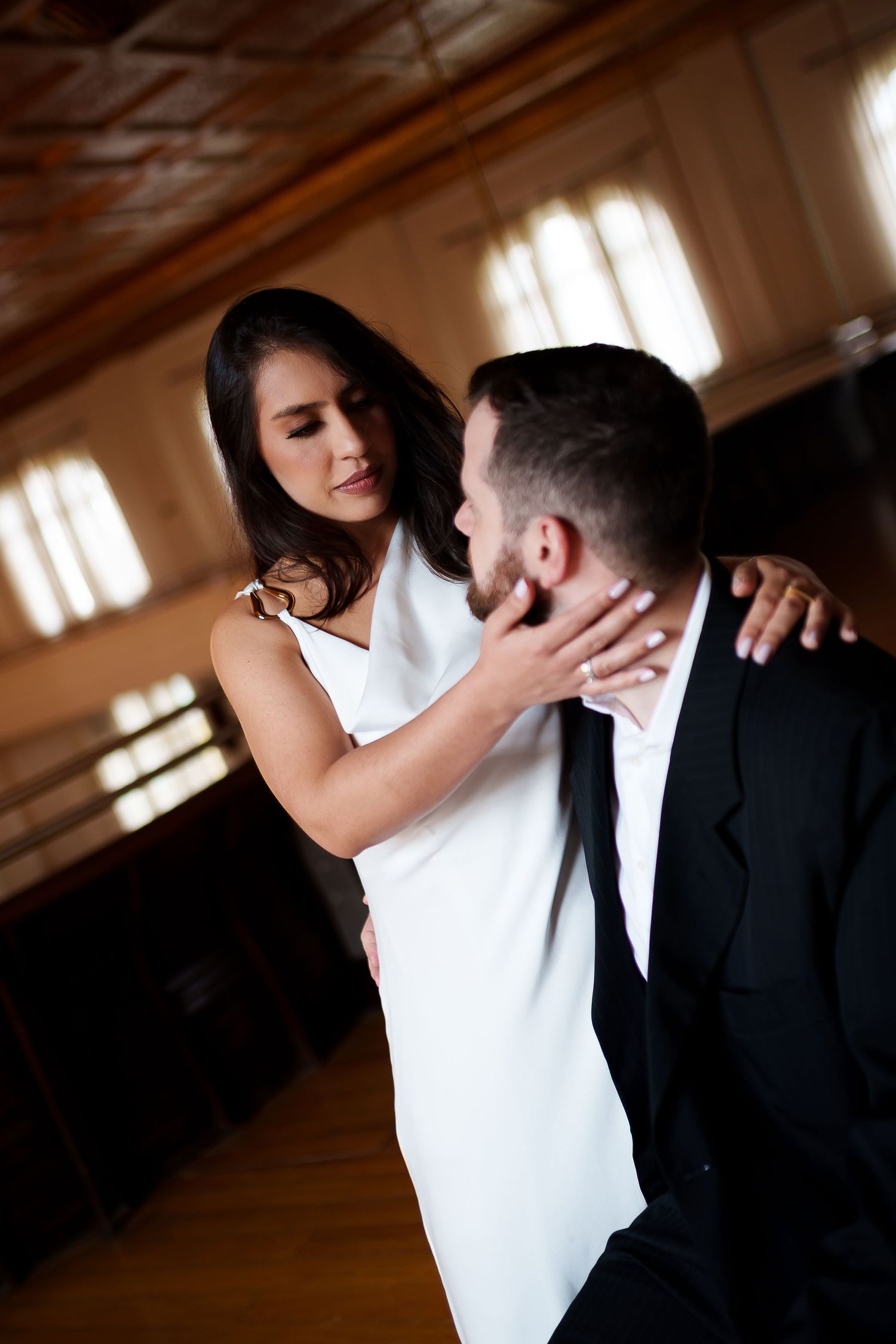 Elegant couple dancing intimately, woman in white dress touching man's face in formal venue.