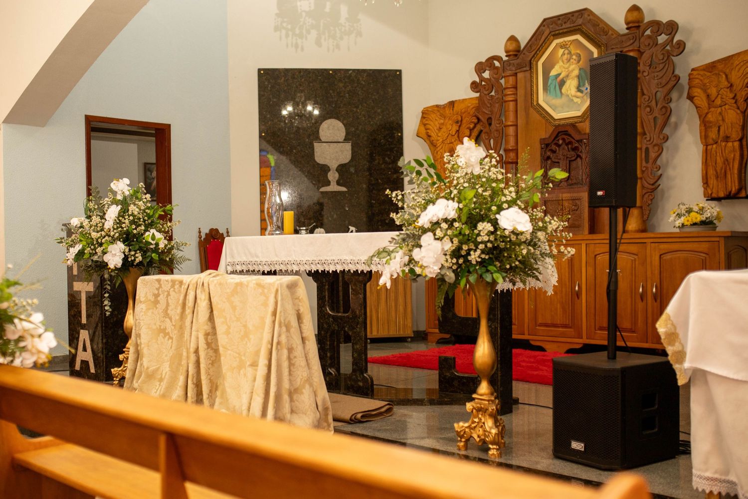 Church altar adorned with white floral arrangements and golden accents, set for a religious ceremony.