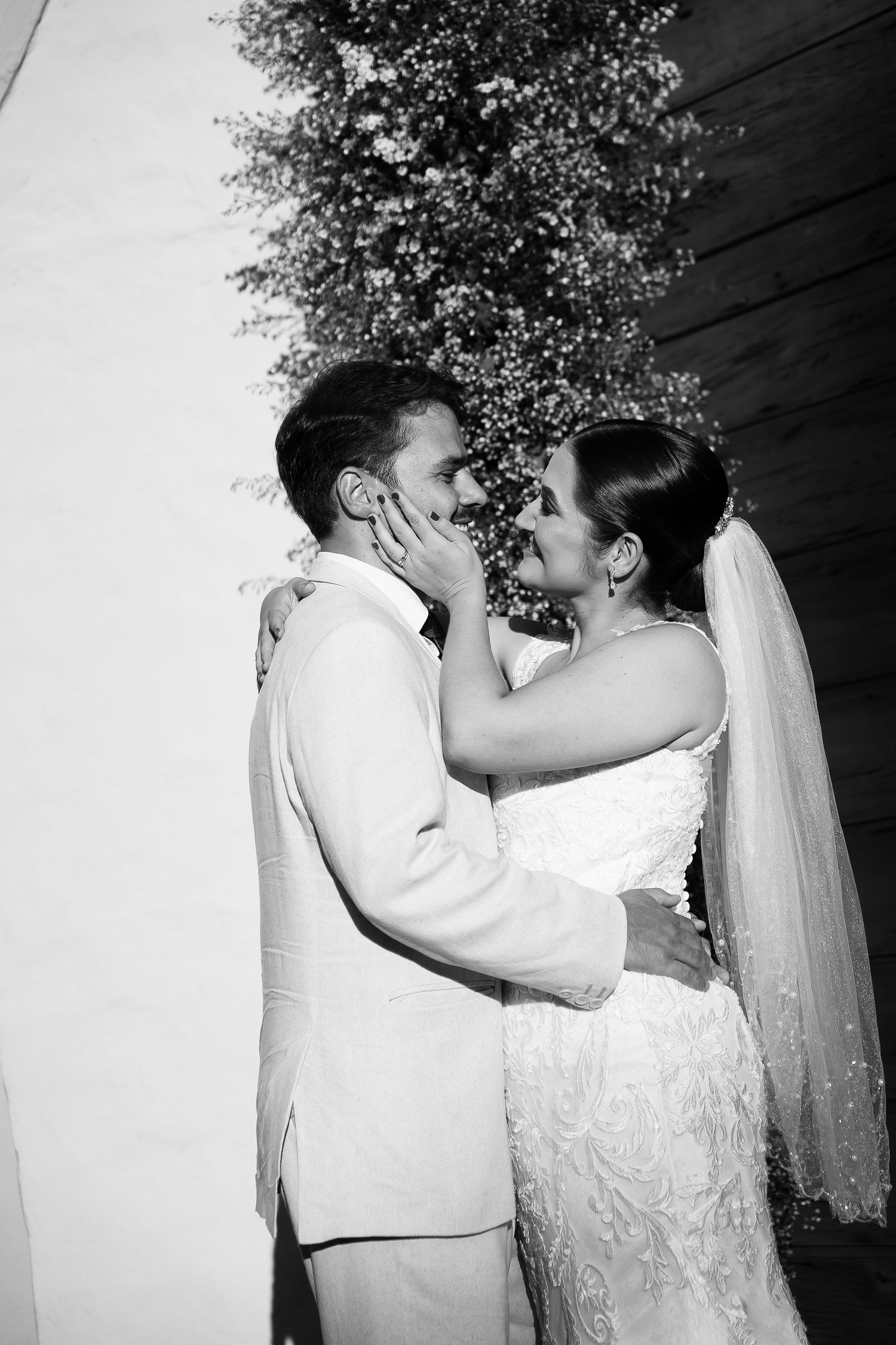 Black and white photo of a bride and groom sharing a romantic moment, with the bride gently holding the groom's face.