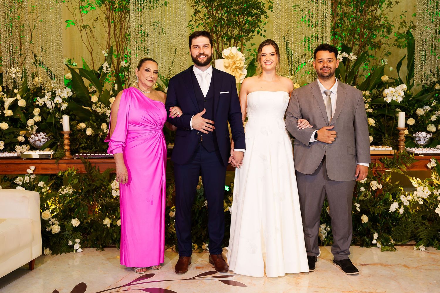 Wedding party poses elegantly in formal attire, featuring a bride in white gown with guests in pink and gray suits.