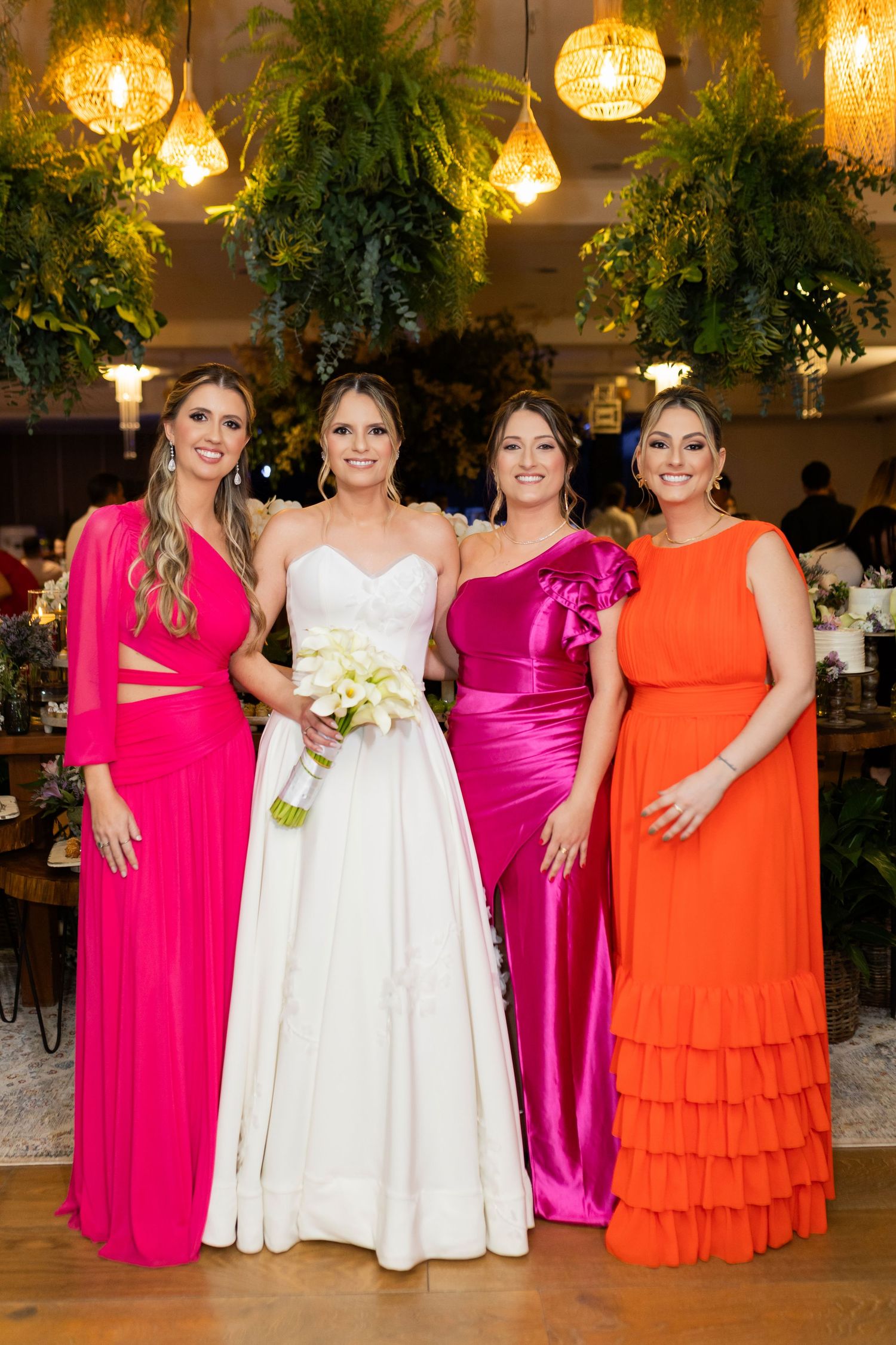 Bride in white gown poses with three bridesmaids in vibrant pink and orange dresses at elegant wedding reception.