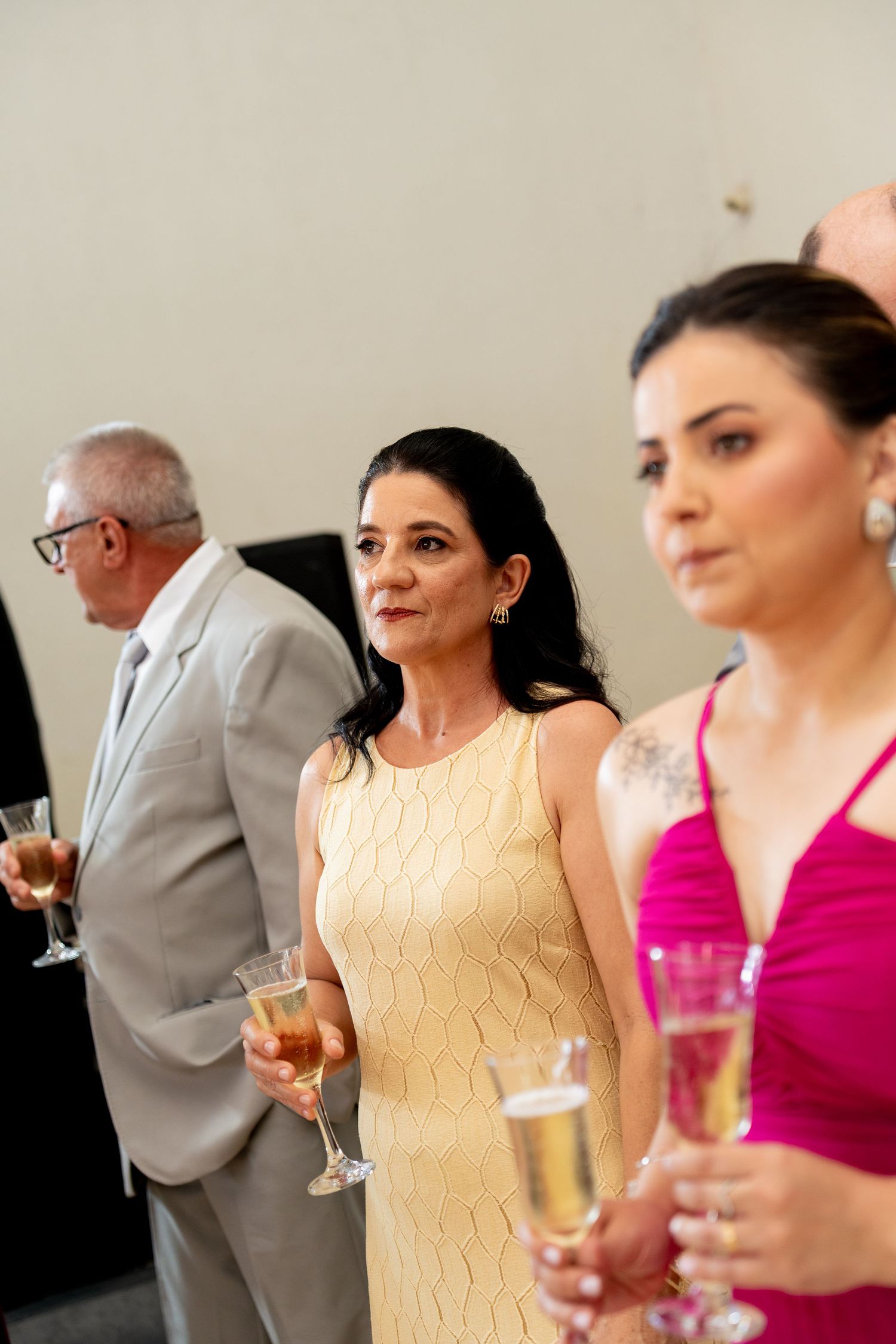 Elegantly dressed guests holding champagne glasses at a formal event, wearing yellow and pink dresses.