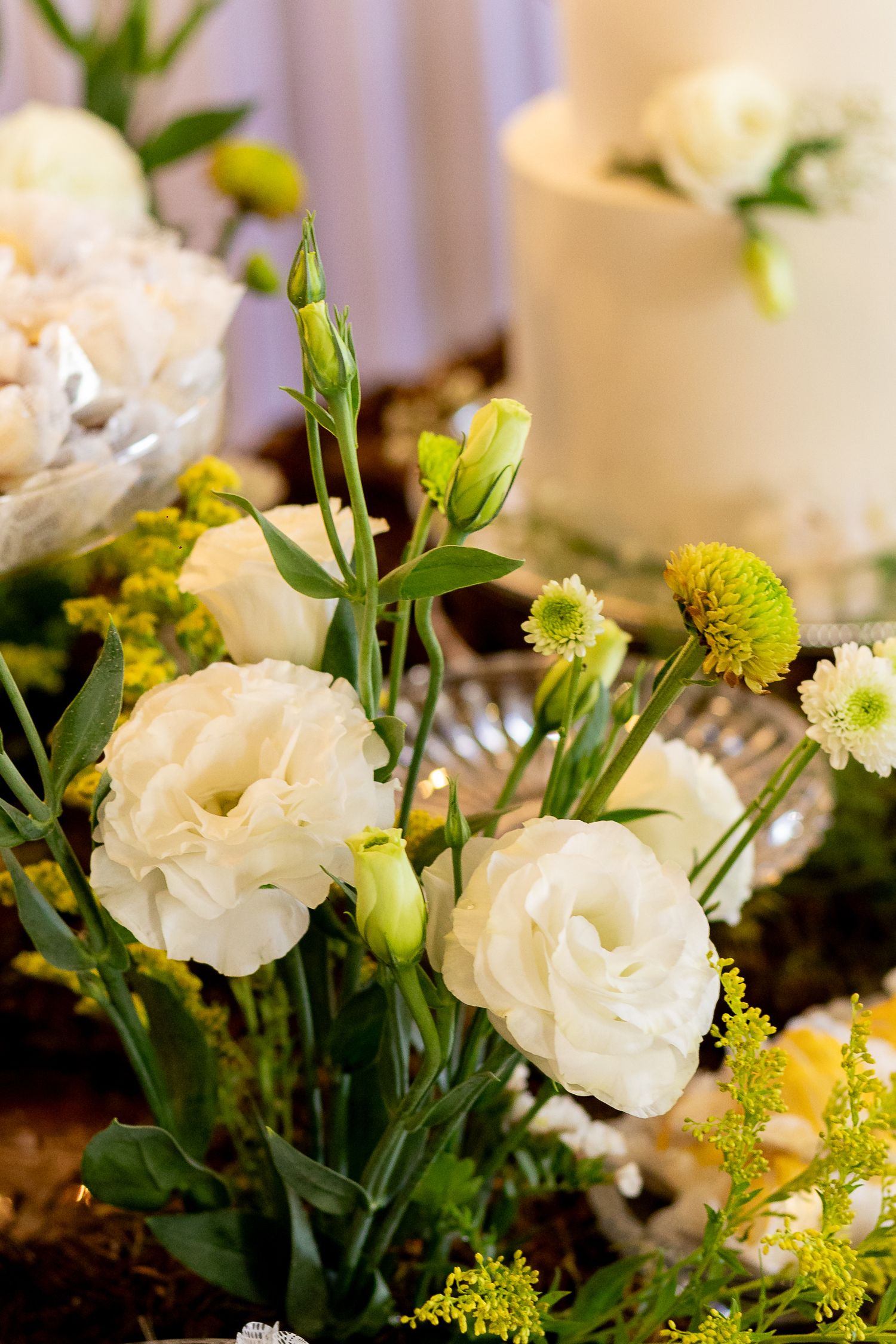 White lisianthus and green mums floral arrangement with a white wedding cake in the background.