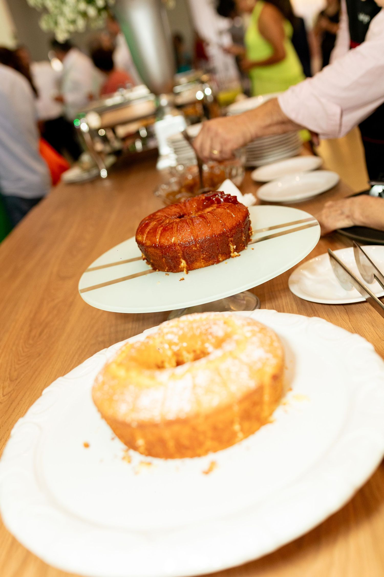Two bundt cakes displayed on white plates at a buffet table, with powdered sugar topping the foreground cake.