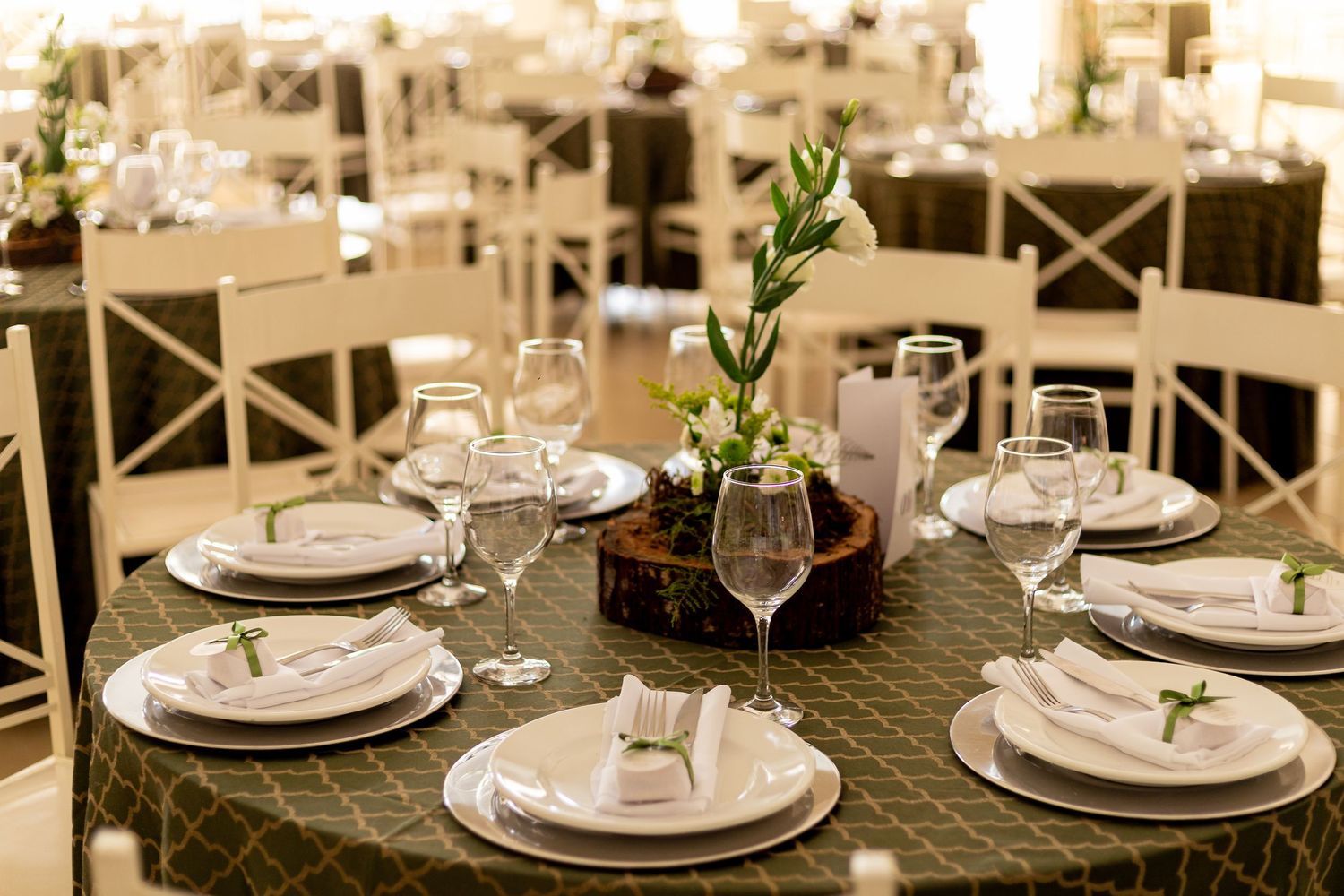 Elegant wedding reception table set with white plates, wine glasses, linen napkins, and a floral centerpiece on a dark tablecloth.