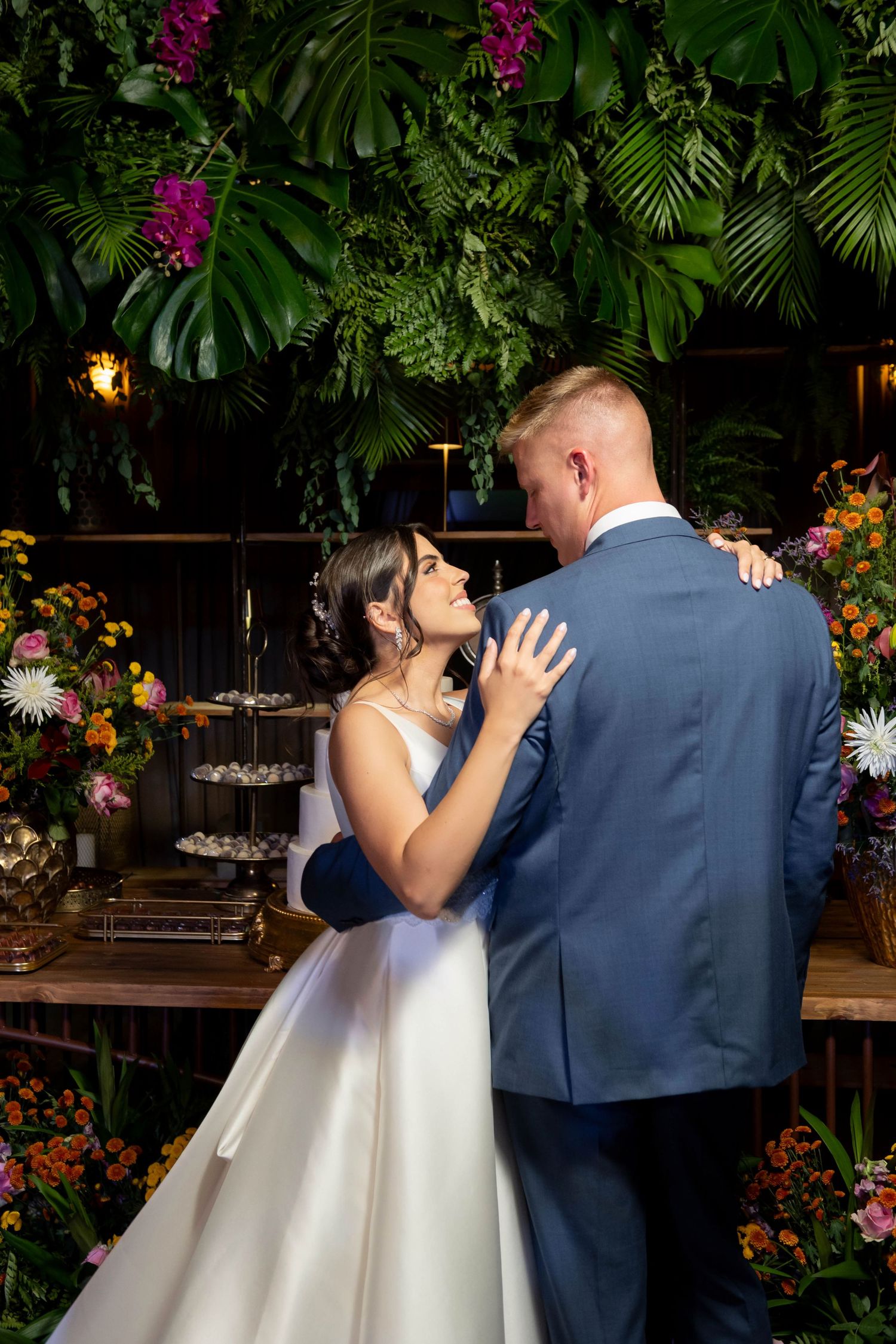 Bride and groom share first dance surrounded by tropical greenery and colorful floral arrangements at wedding reception.
