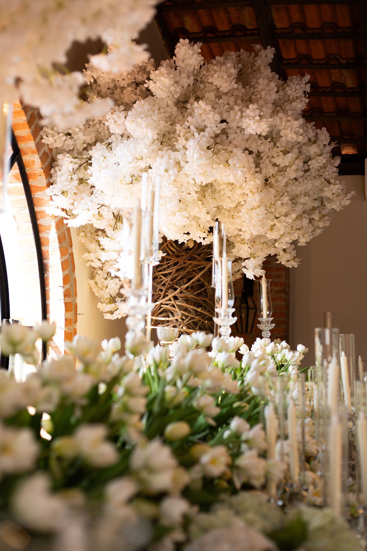 Elegant wedding decor with white floral arrangements, tall candles, and a stunning white blossom tree centerpiece.