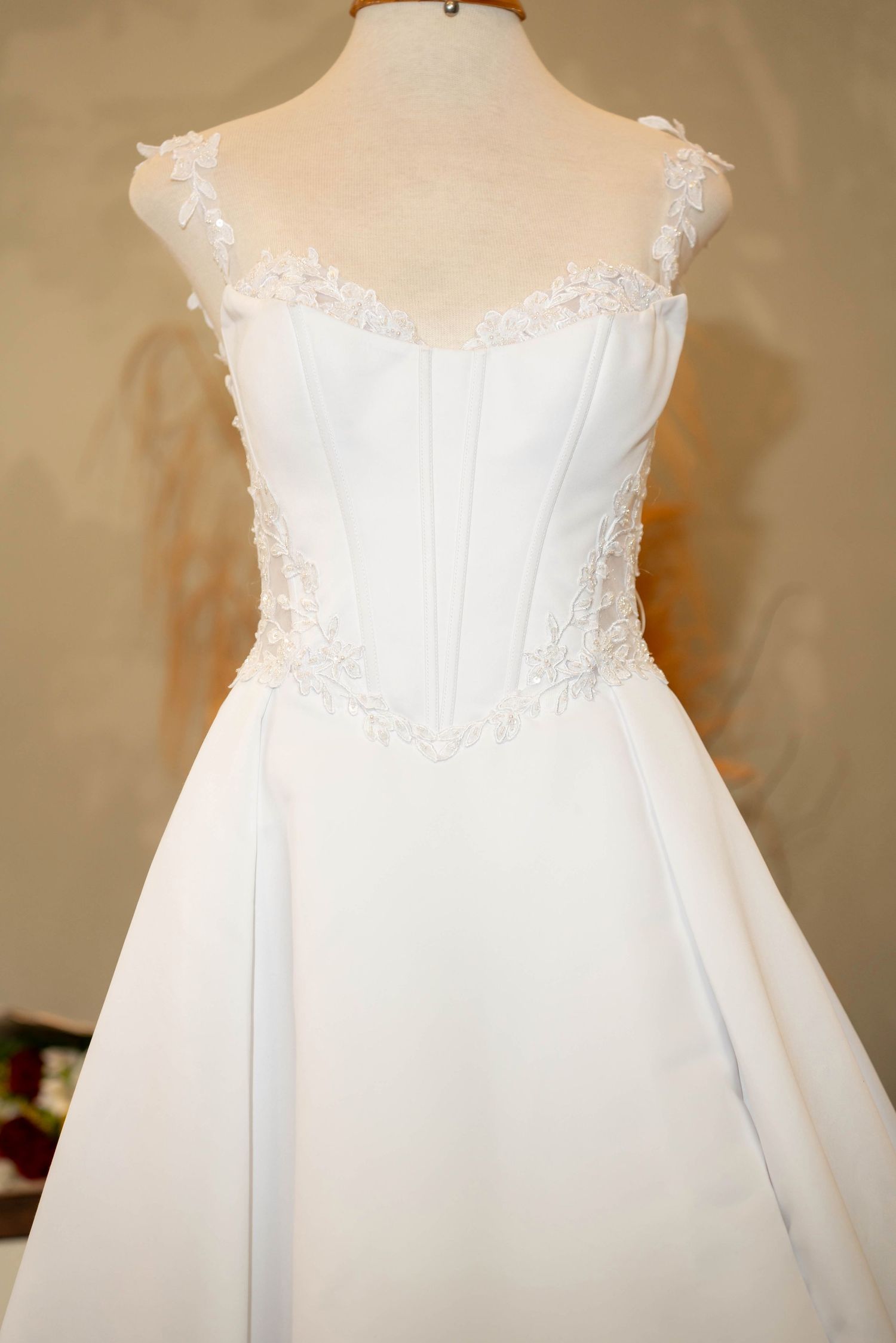 Elegant white bridal gown on mannequin featuring lace floral details, sweetheart neckline, and structured corset bodice.