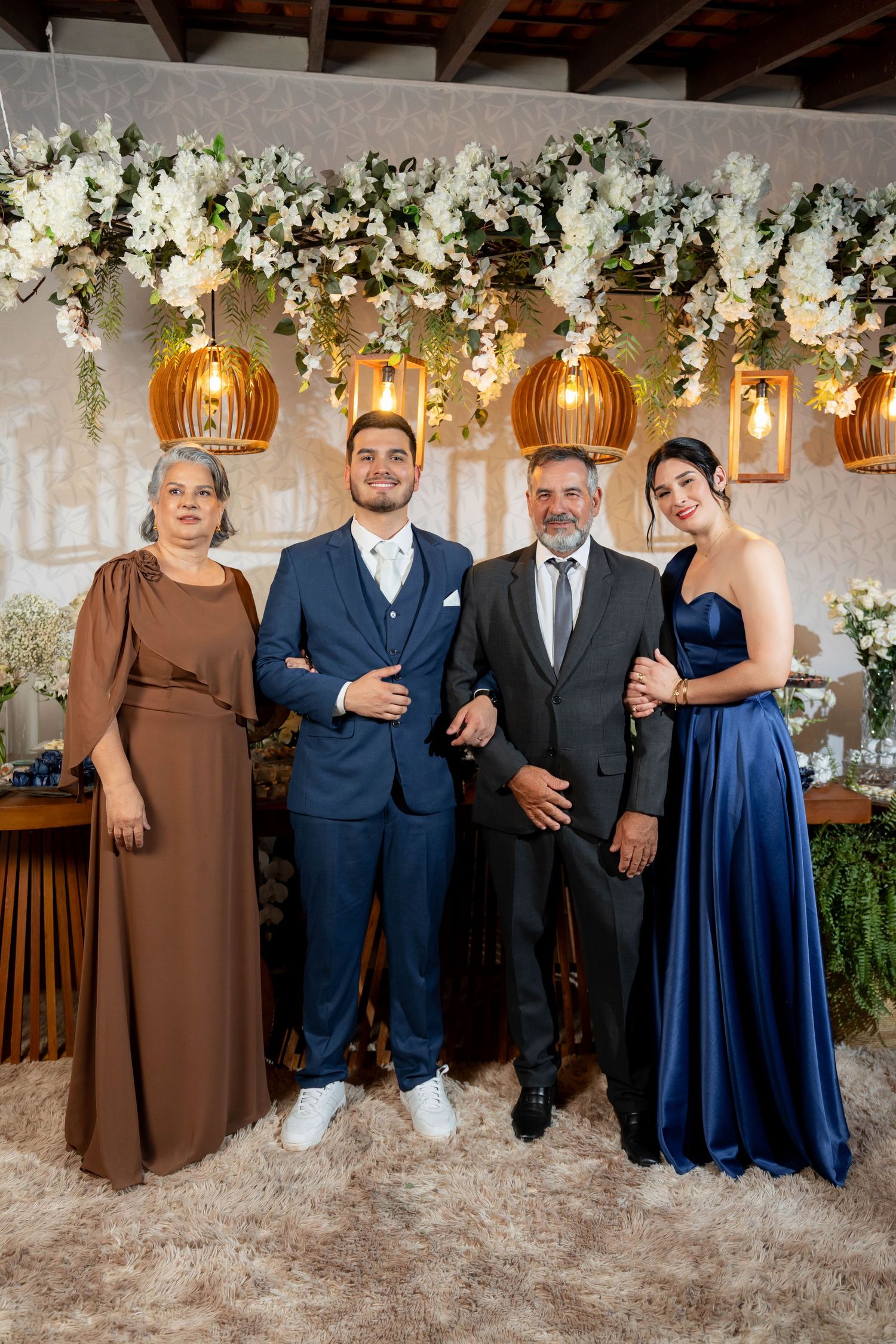 Family of four posing elegantly at a wedding reception, decorated with hanging floral arrangements and warm pendant lights.