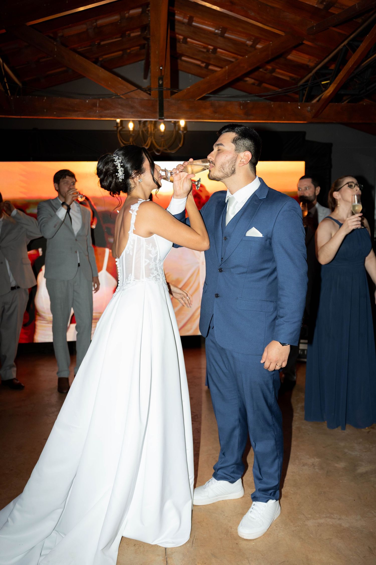 Bride in white gown and groom in navy suit share a champagne toast at their elegant wedding reception.