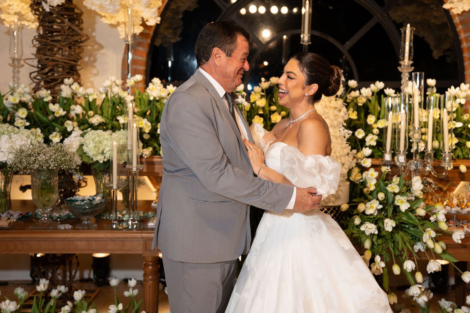 Bride and groom share first dance surrounded by elegant white floral arrangements and candlelight at a wedding reception.