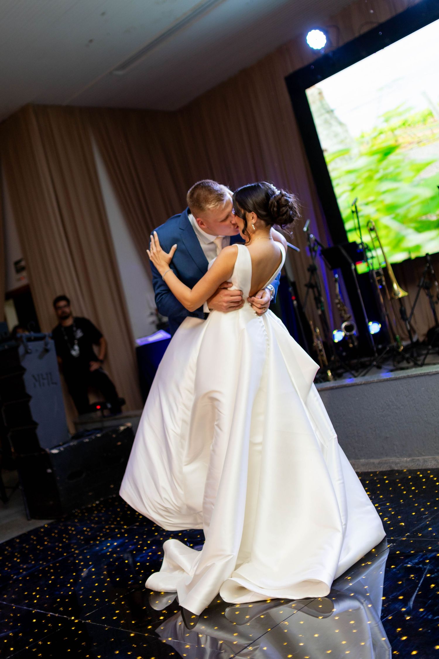 Bride and groom share their first dance kiss in elegant ballroom, bride wearing stunning white ball gown.