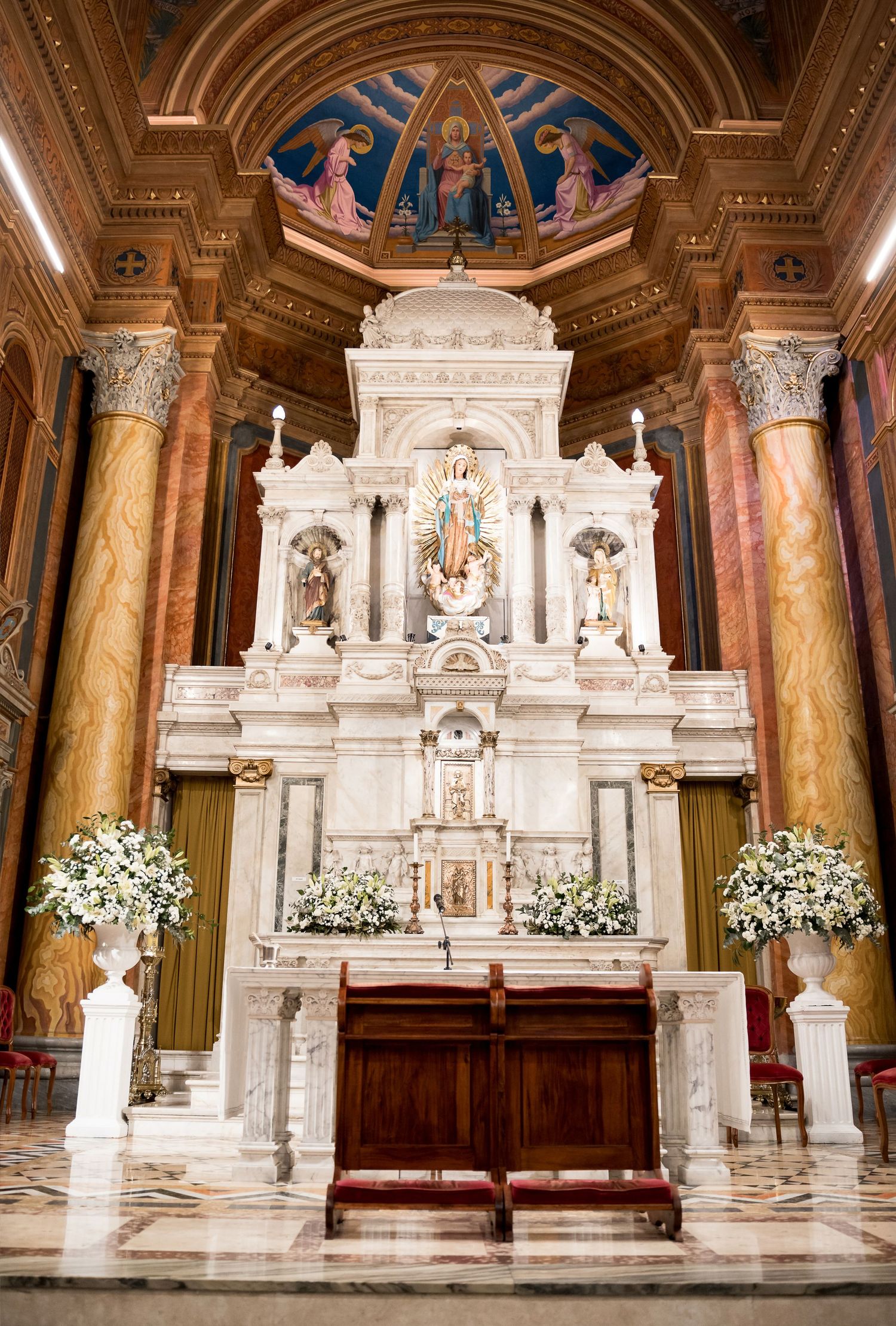 Ornate white marble altar with floral arrangements in an elegant cathedral with golden columns.