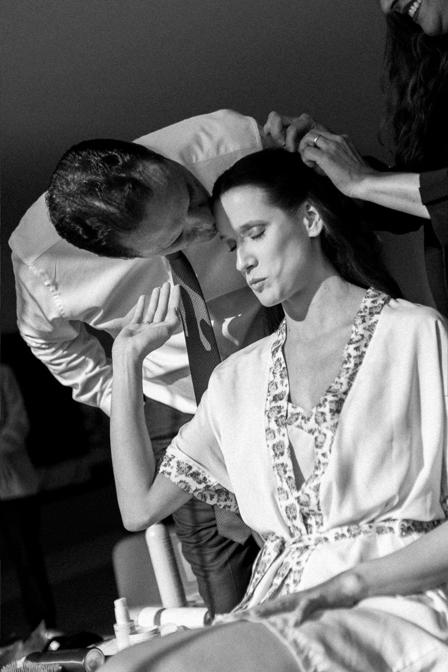 Black and white photo of a model getting hair and makeup done backstage before a fashion show.