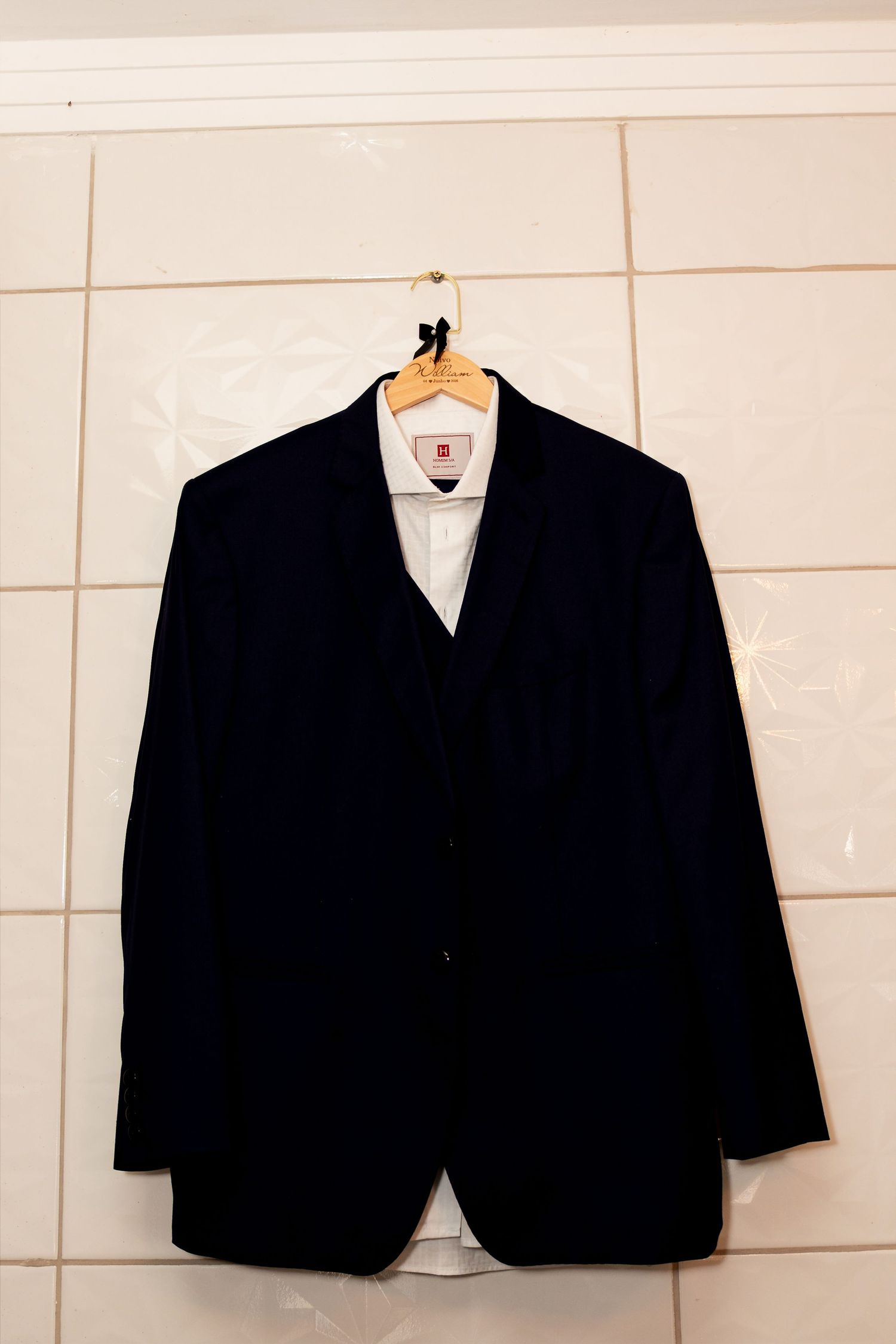 Dark navy suit jacket on wooden hanger against white tiled wall.