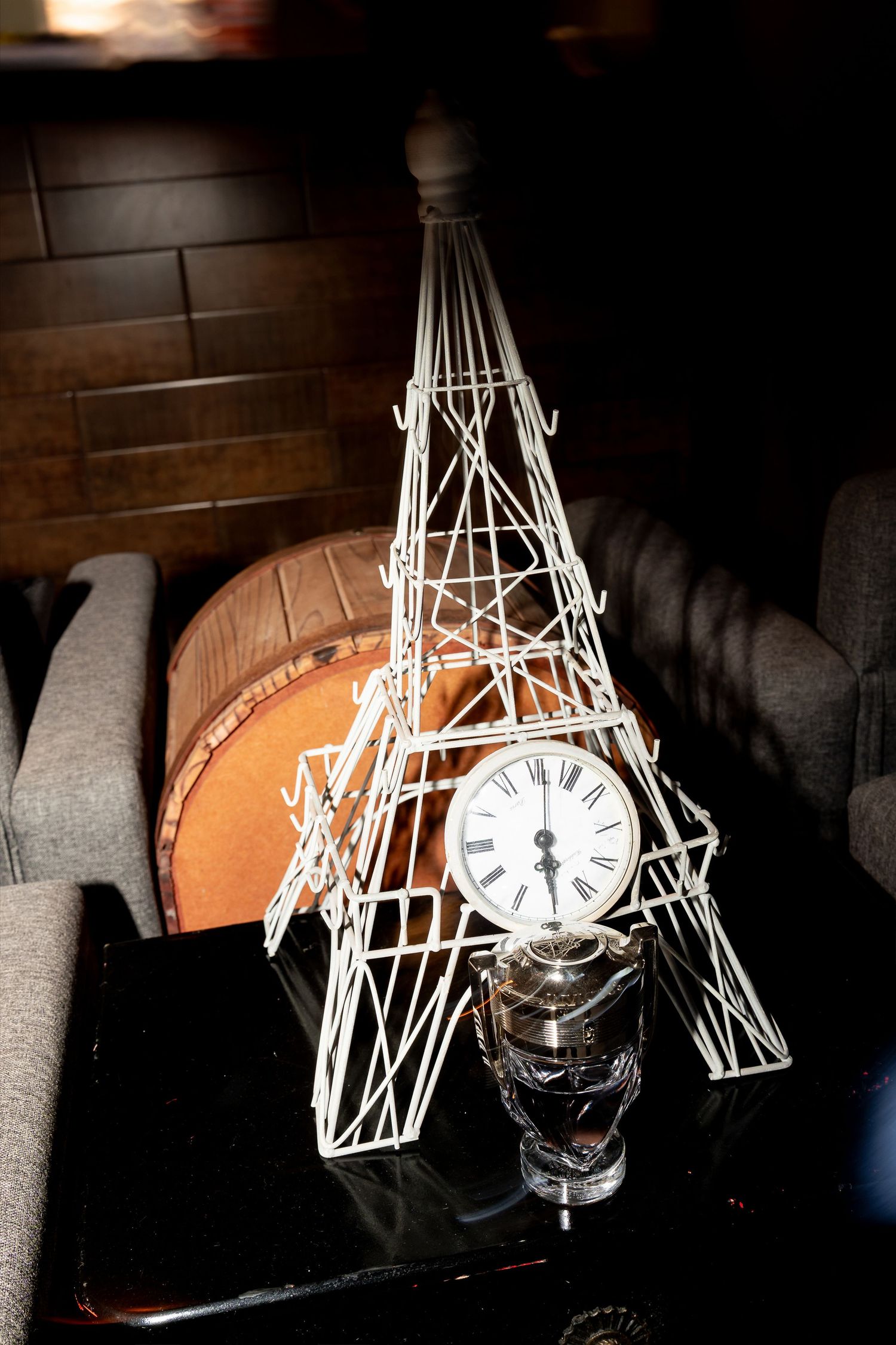 Decorative wire Eiffel Tower model with vintage Roman numeral clock base on dark table.