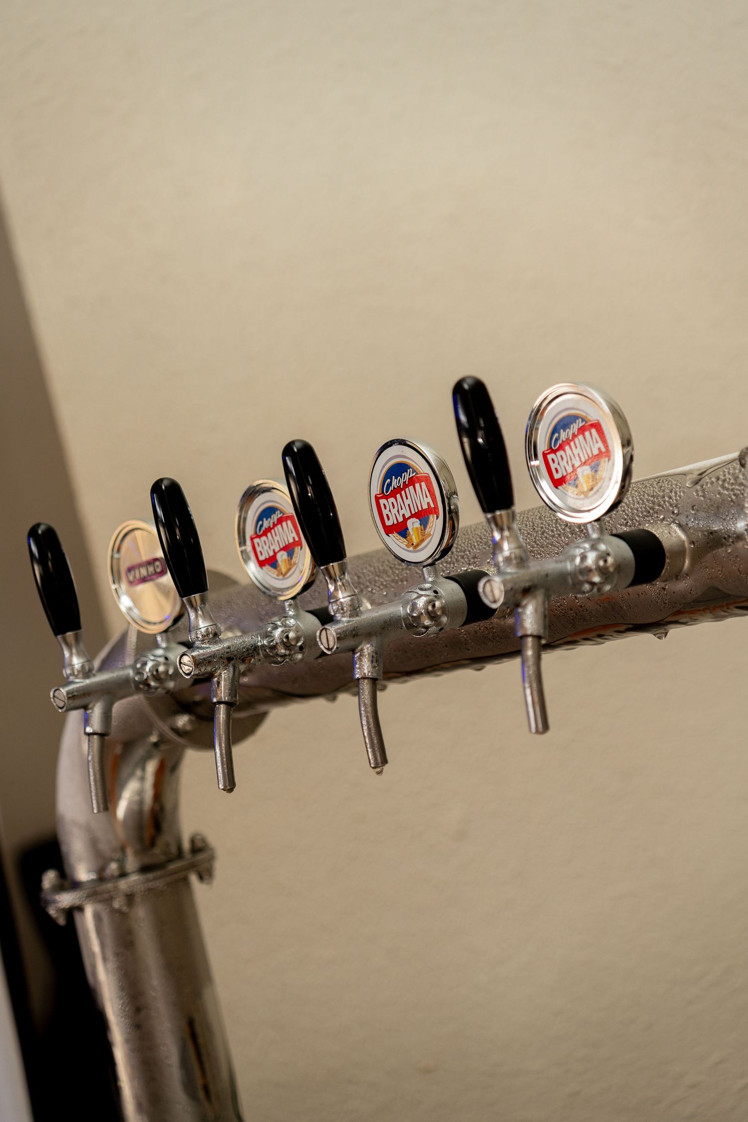 Four Brahma beer tap handles mounted on a stainless steel draft beer tower against a beige wall.