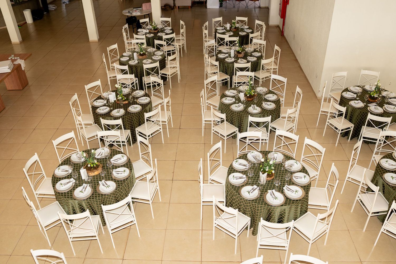 Elegant banquet hall with round tables draped in green tablecloths, white chiavari chairs, and formal place settings.