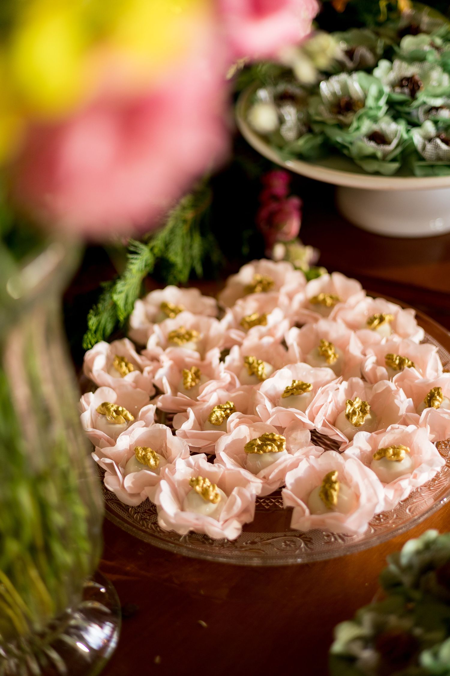 Elegant pink flower-shaped meringue cookies with gold centers displayed on a decorative plate at a wedding dessert table.