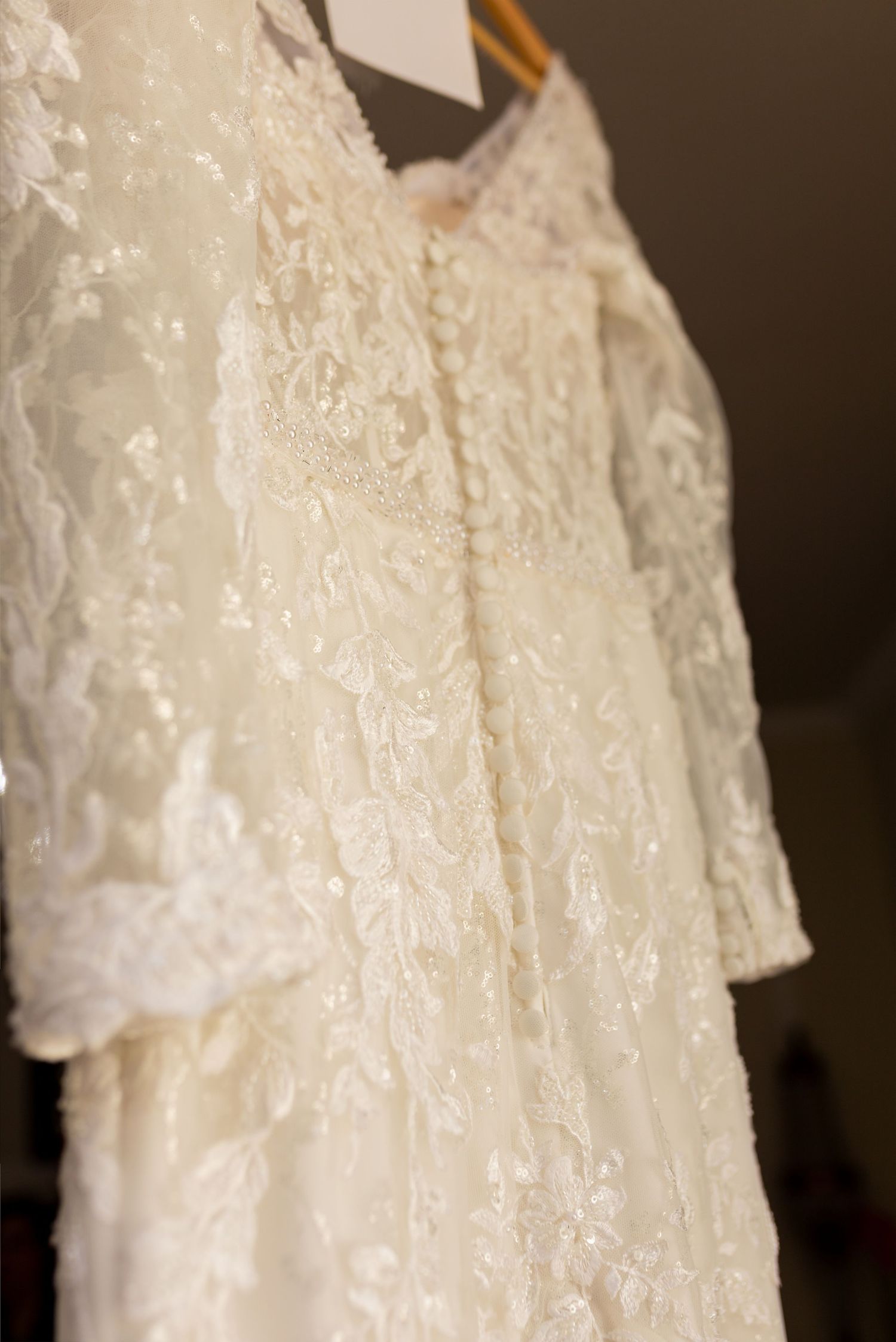 Elegant ivory lace wedding dress with long sleeves and delicate button back detail, hanging on a wooden hanger.