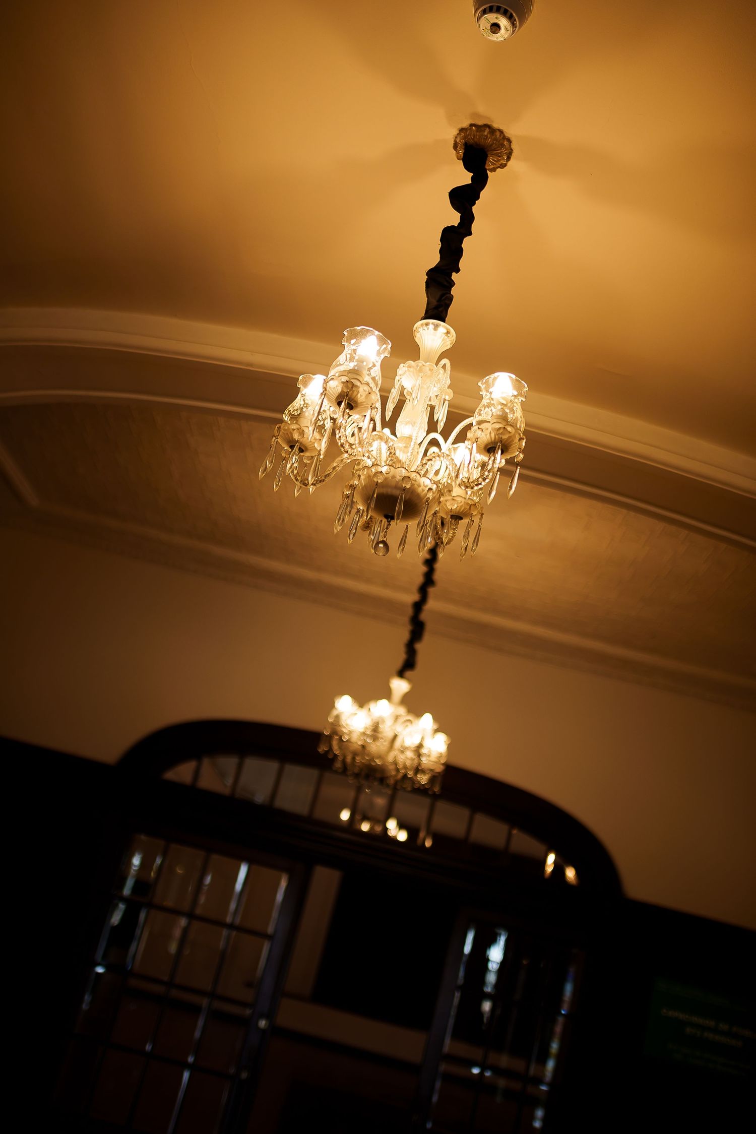 Elegant crystal chandeliers hanging from an ornate ceiling, casting warm golden light in a classic interior.