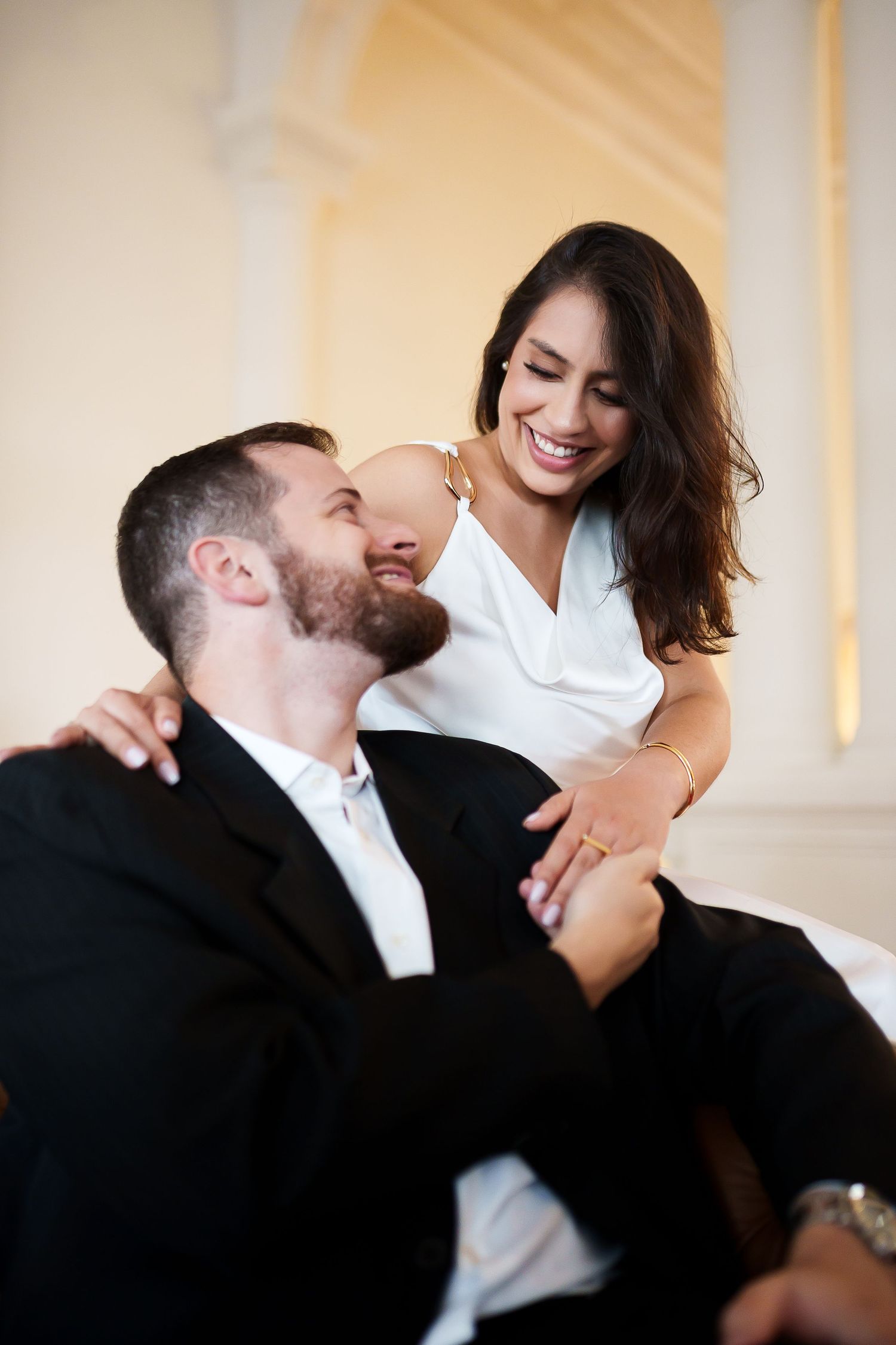 Smiling couple in elegant attire sharing a joyful intimate moment, woman in white dress, man in black suit.