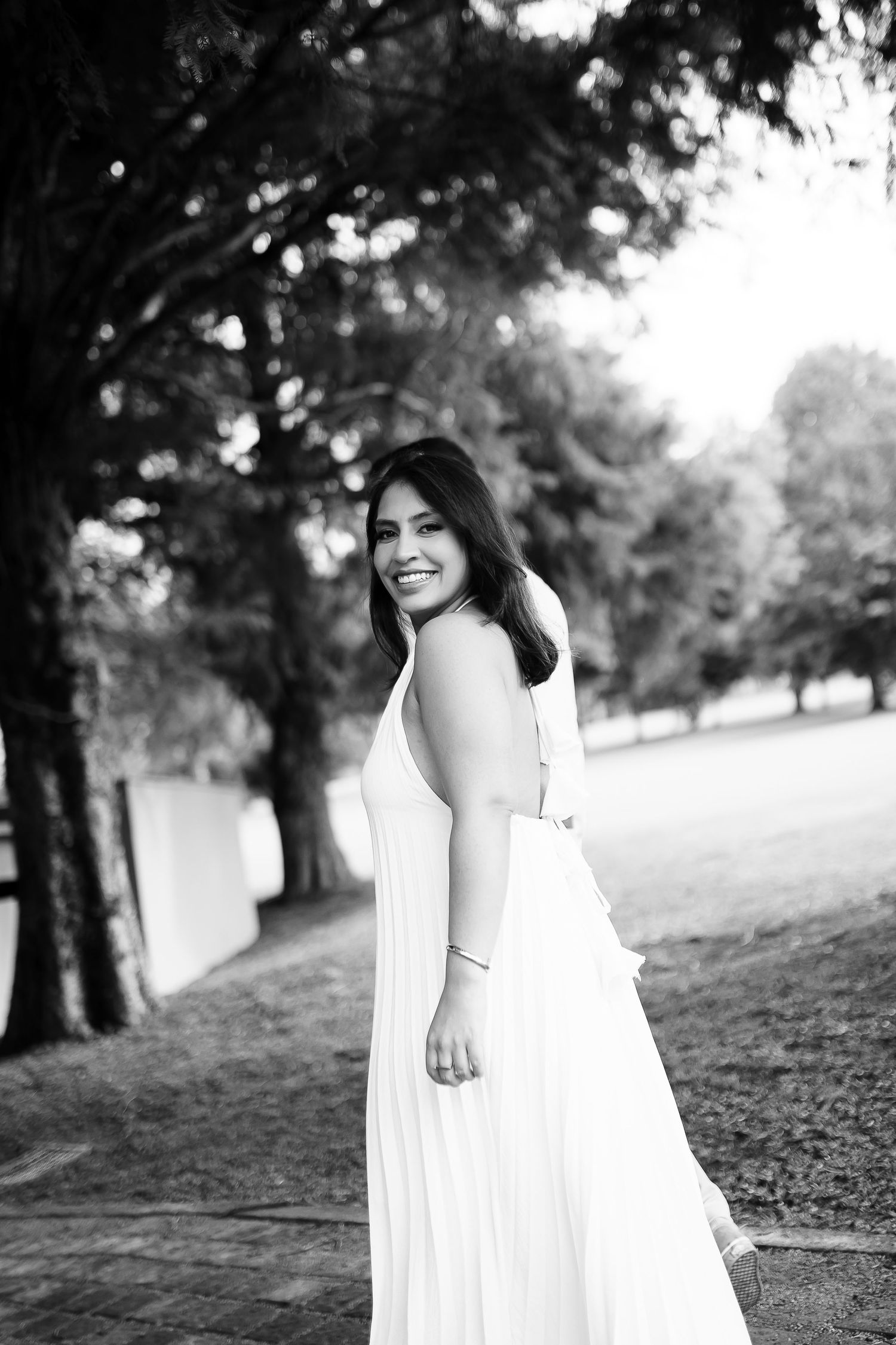 Black and white portrait of smiling woman in white dress in park.