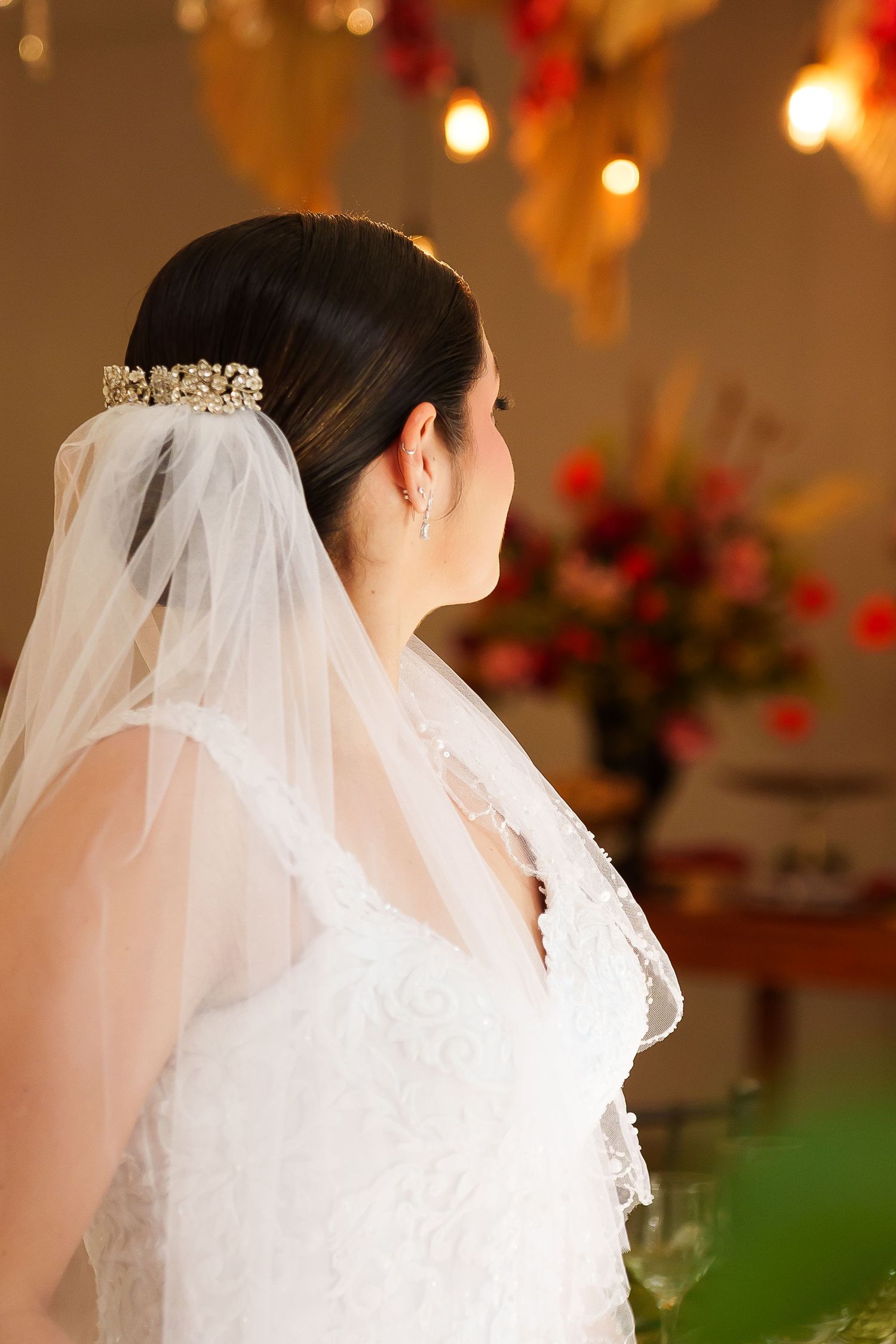 Bride in white lace gown and veil with gold tiara, viewed from behind at wedding reception.
