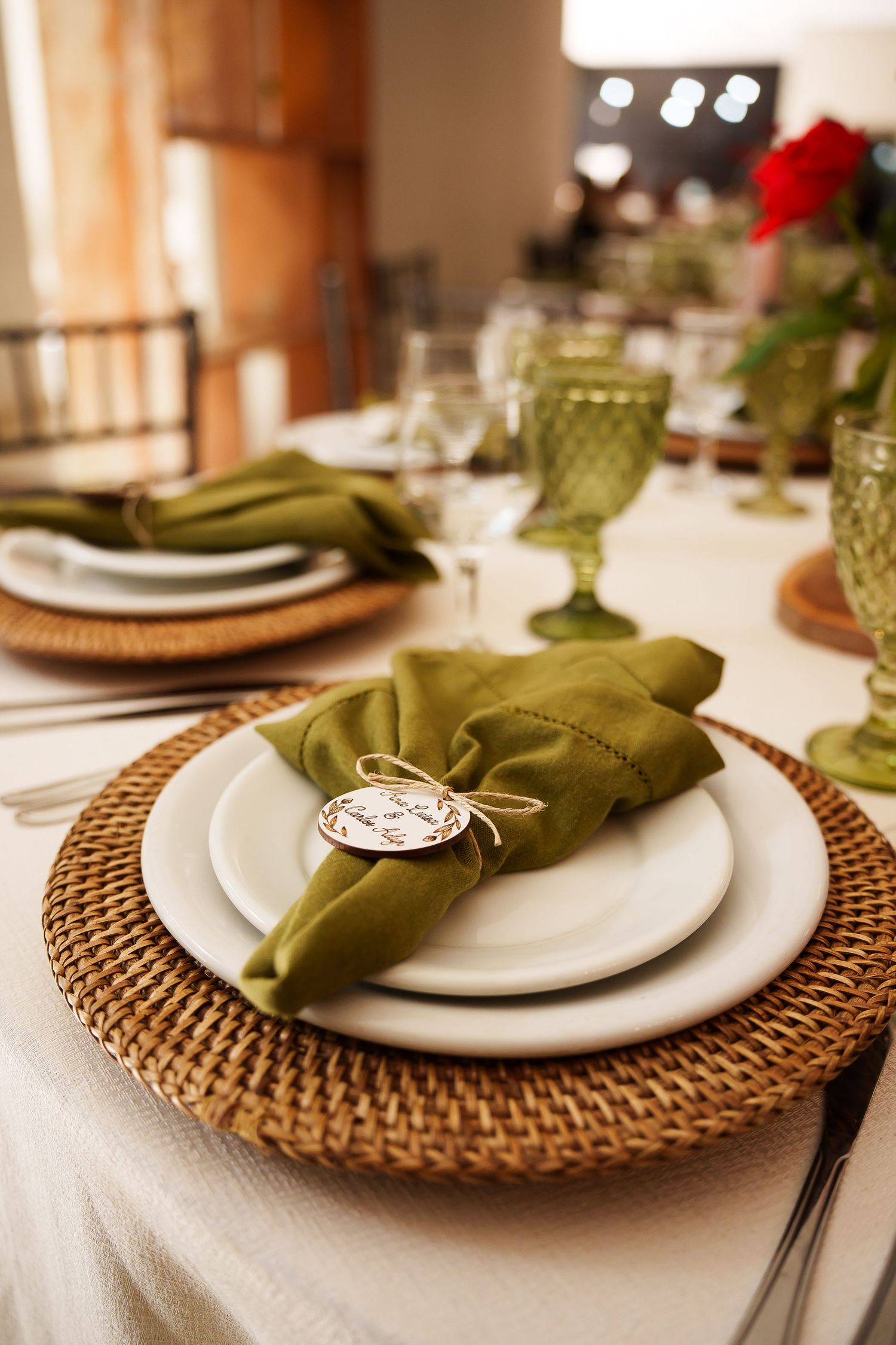 Elegant table setting with green linen napkin, wicker charger plate, and green goblets for a wedding reception.