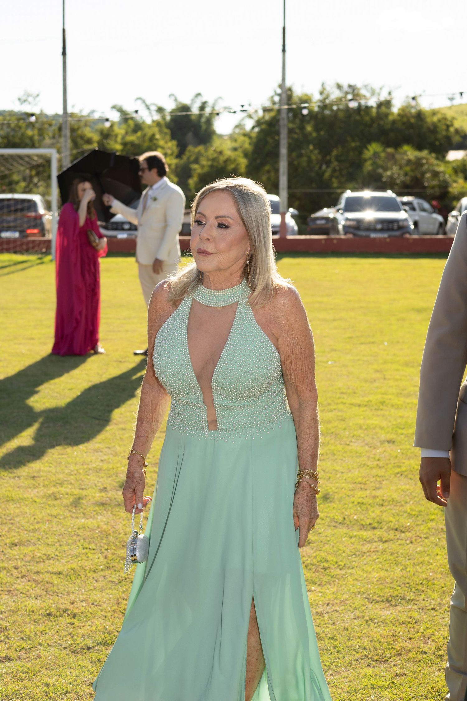 Elegant woman in a mint green halter gown with pearl details walks on grass at an outdoor formal event.