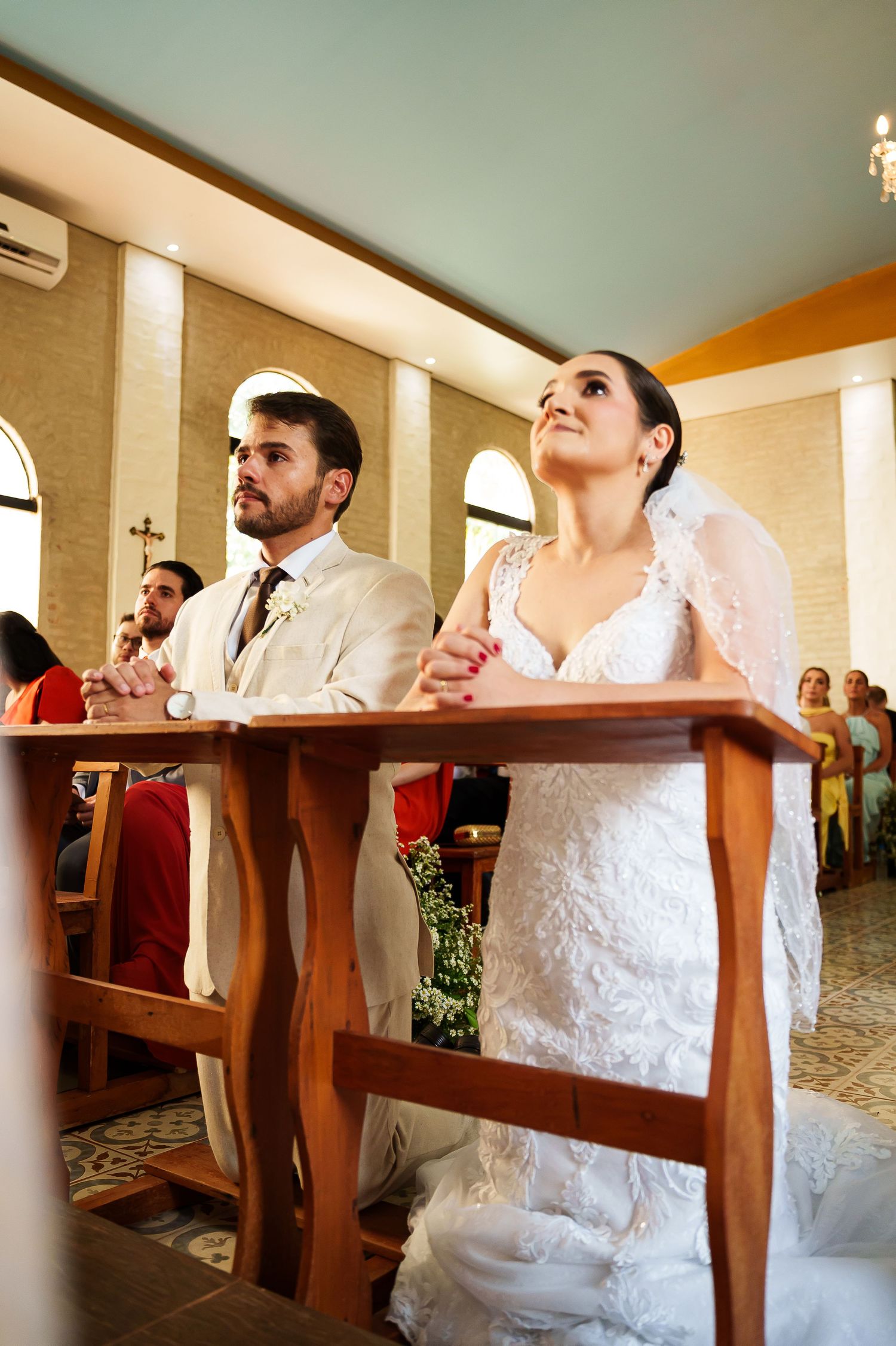 Bride and groom kneeling at church altar during wedding ceremony, bride in white lace gown with veil.