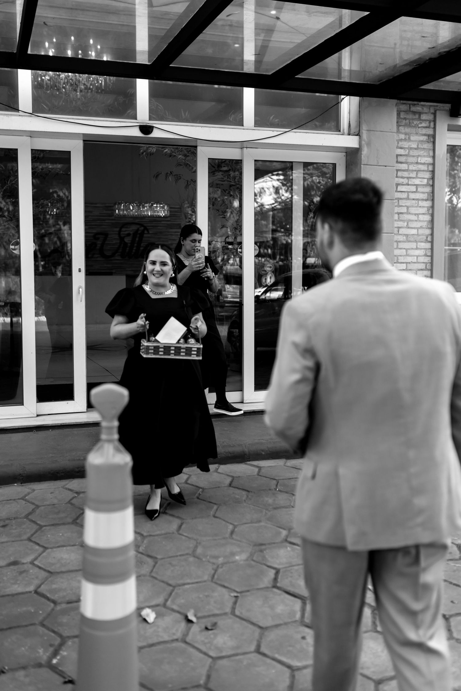 Black and white photo of a smiling woman in a black dress greeting a man in a suit outside a building.