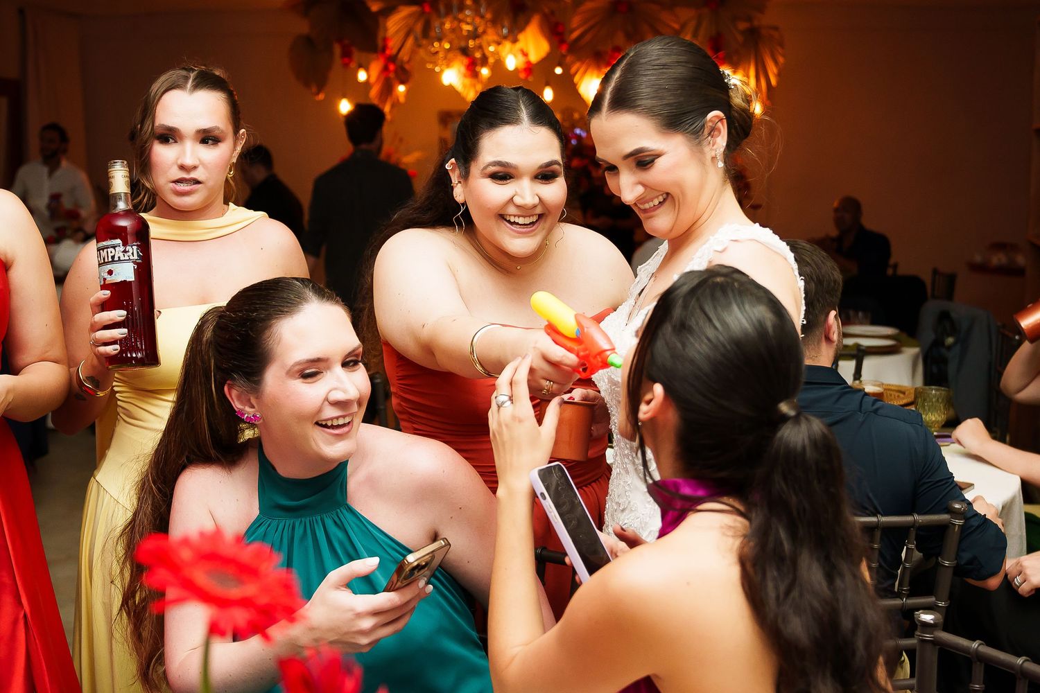 Bridesmaids in colorful dresses laughing and taking photos together at a festive wedding reception.