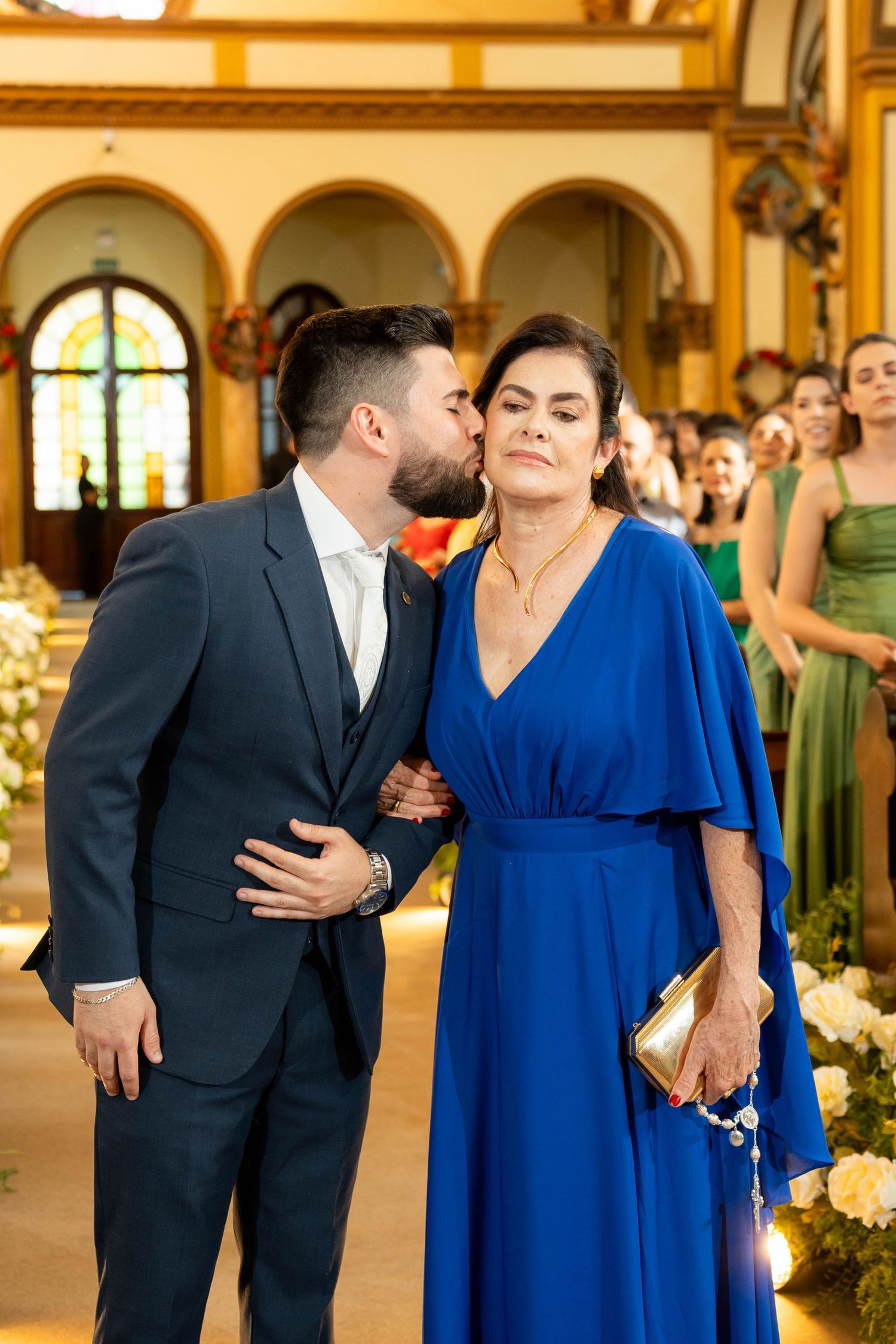 Groom in navy suit kisses woman in royal blue gown at elegant church wedding ceremony.