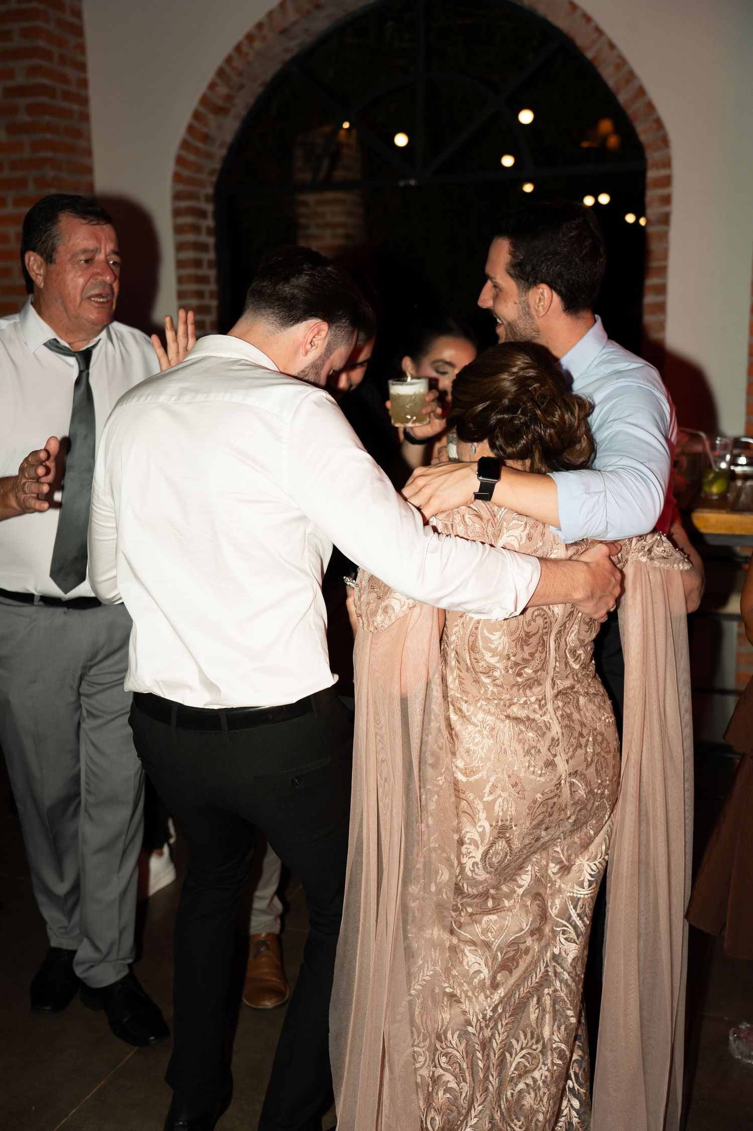 Guests in formal attire embracing and dancing together at an elegant wedding reception venue.