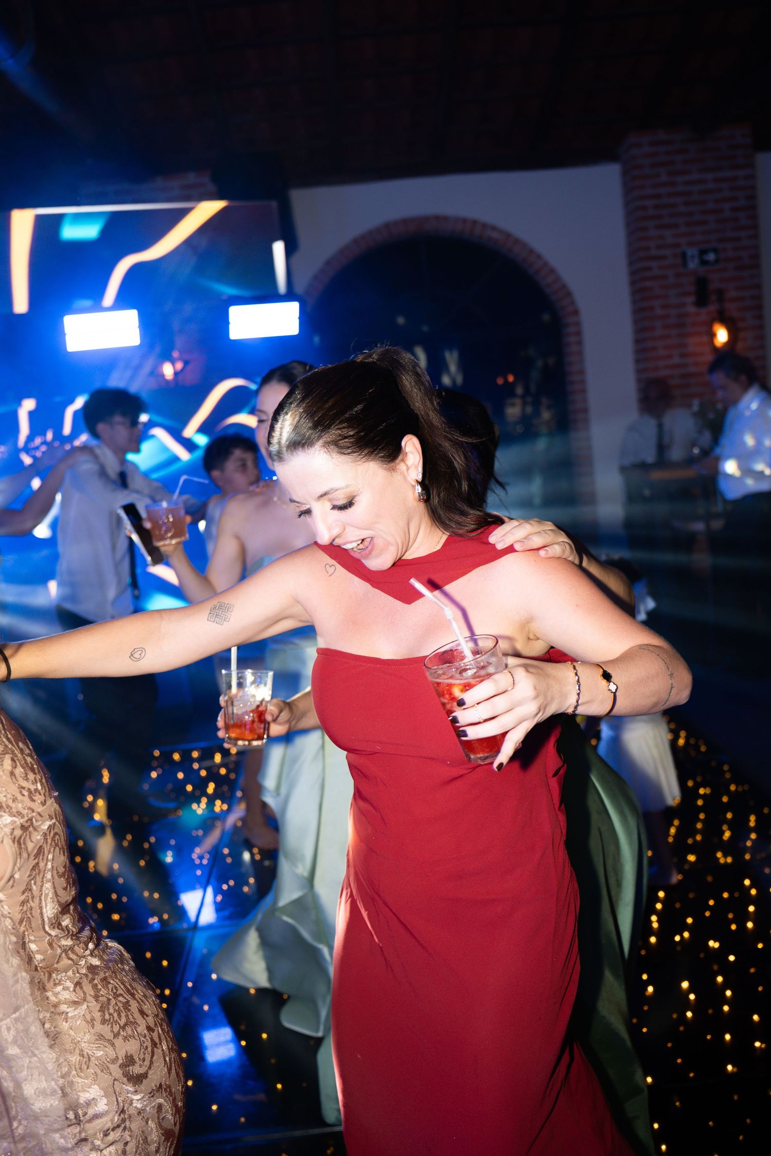Woman in red dress dancing at a nightclub party, holding a cocktail drink, with blue lights in the background.
