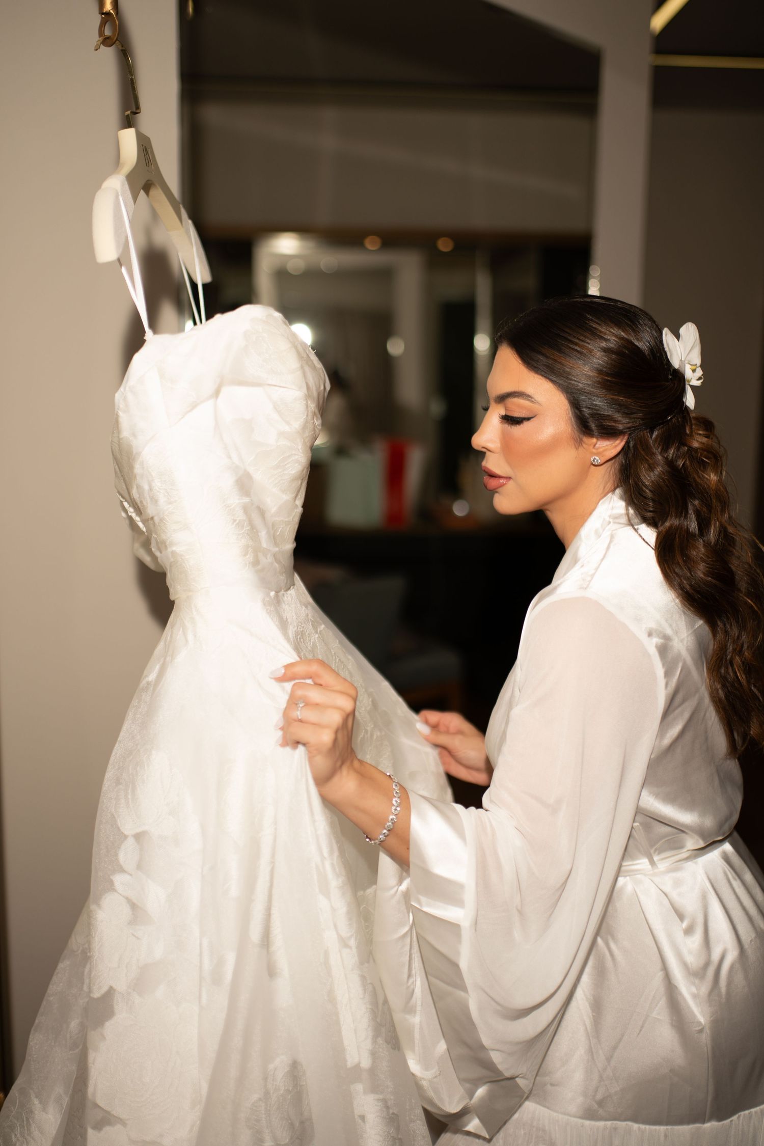 Bride in white robe admiring her wedding dress on a hanger before the ceremony.