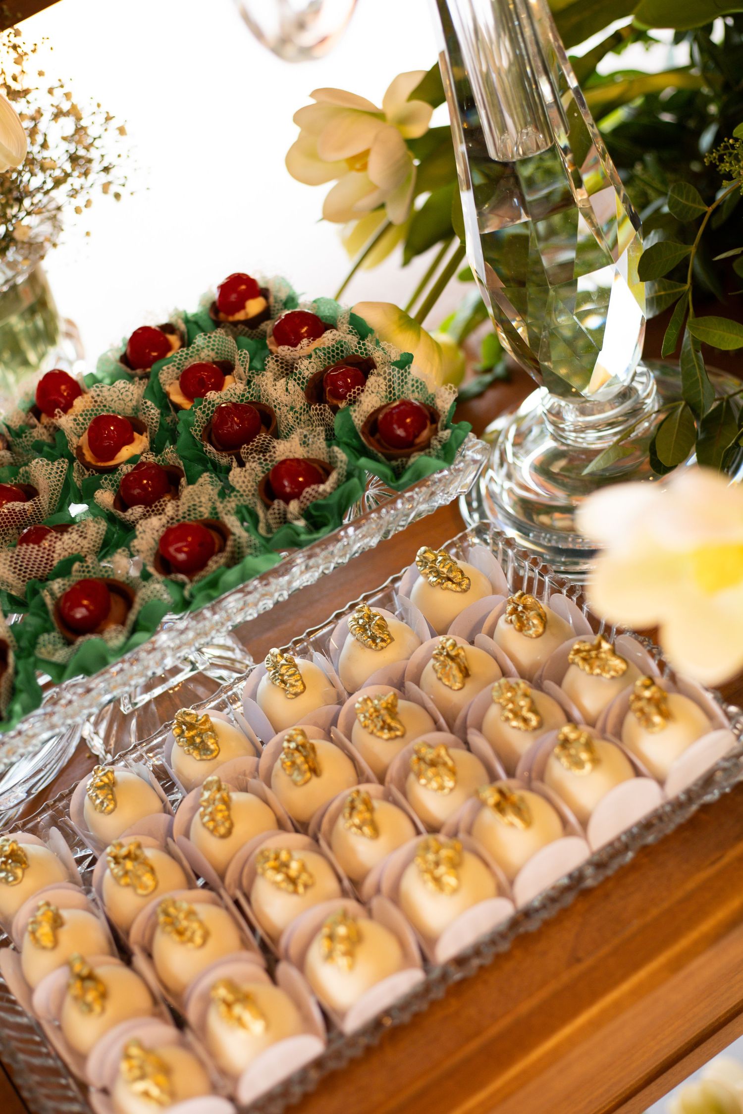 Elegant dessert table with gold-topped truffles and cherry chocolates in green cups, arranged on crystal trays.