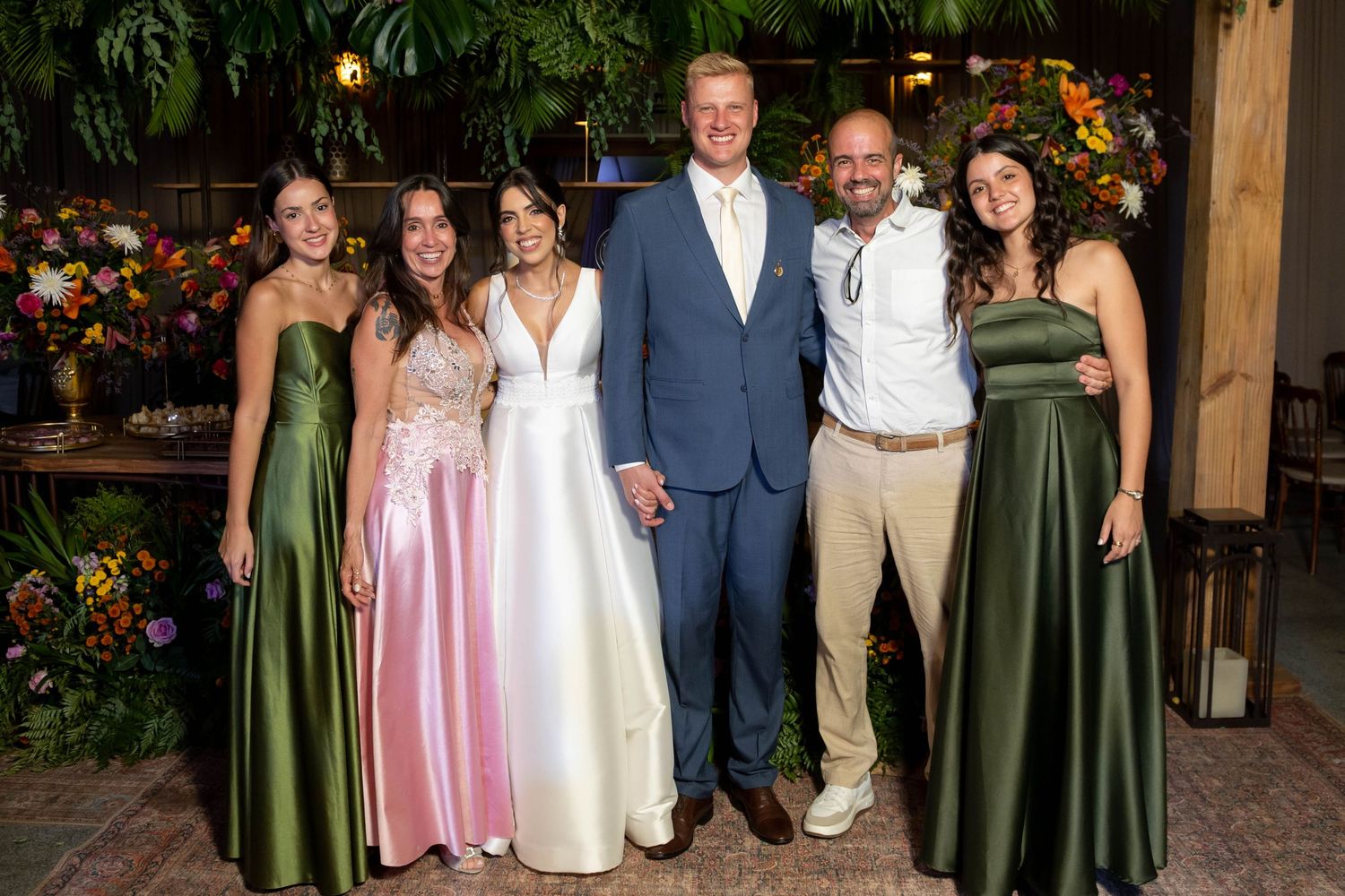 Wedding party poses together, bride in white gown, groom in blue suit, bridesmaids in green and pink dresses.