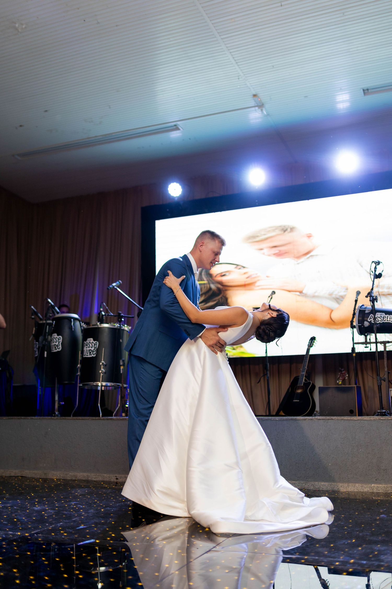 Bride and groom share romantic first dance dip at elegant wedding reception with stage lighting.