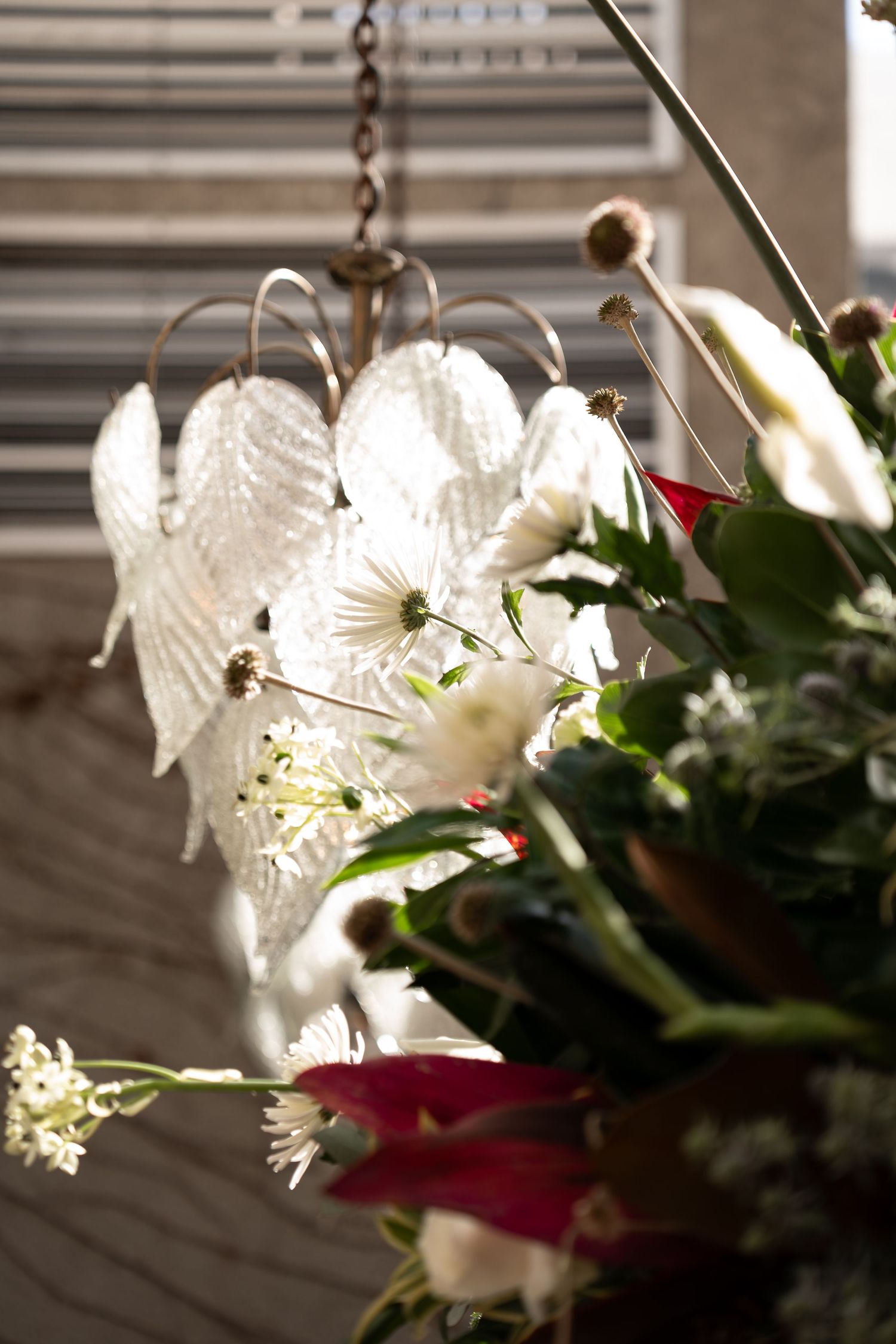 Elegant glass leaf chandelier hanging near a lush floral arrangement with white and red blooms in natural light.