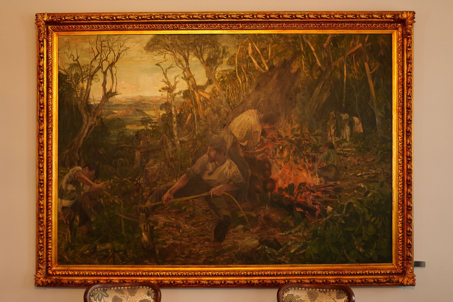 Antique oil painting in gold frame depicting figures clearing land with fire in a dense tropical forest setting.