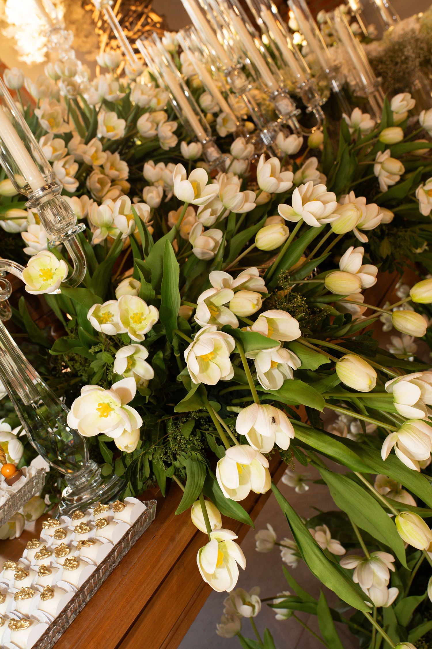Elegant white tulip floral arrangement with green foliage and crystal candelabras at a formal event.