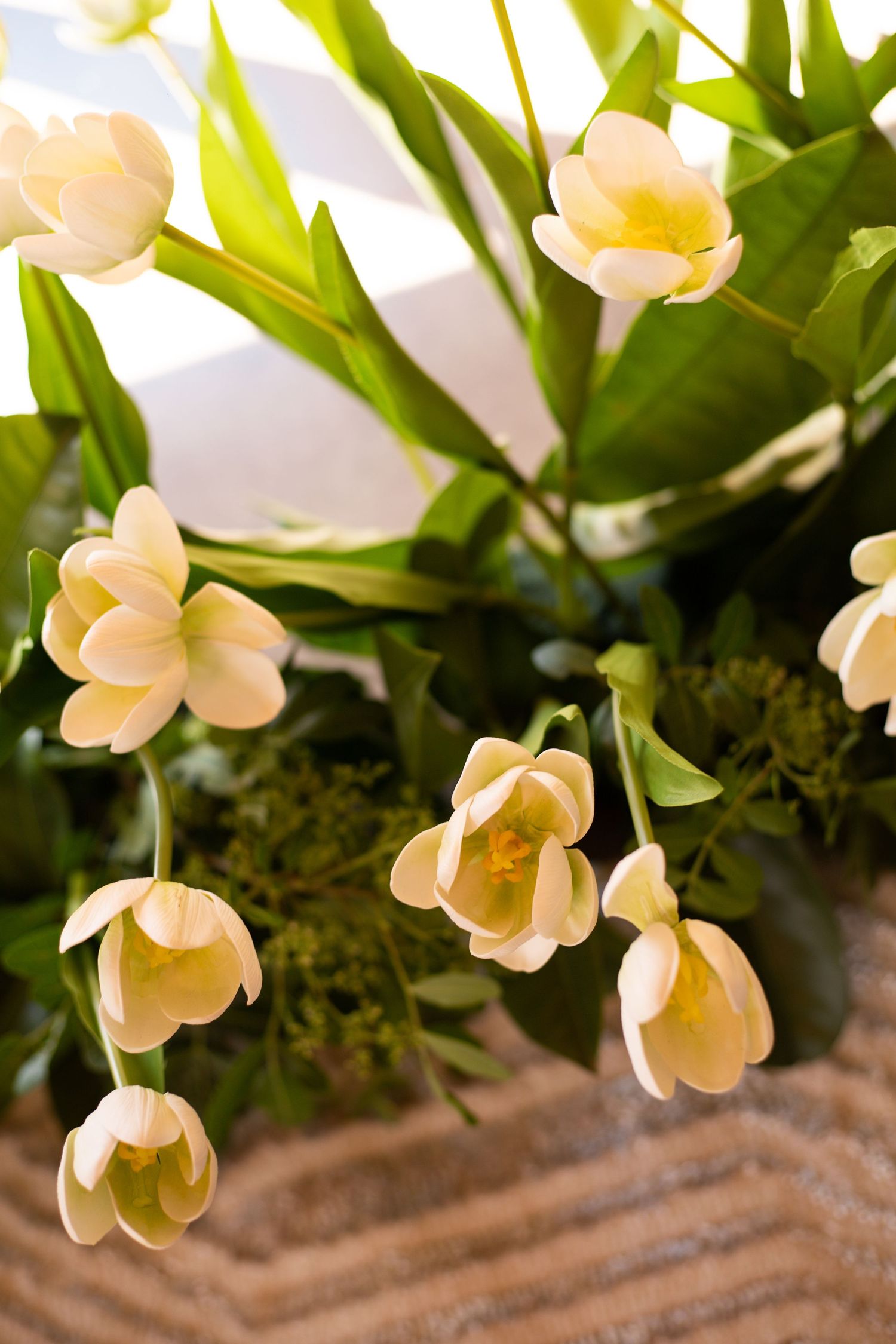 Delicate white tulips with green leaves arranged in a wicker basket, bathed in soft natural sunlight.
